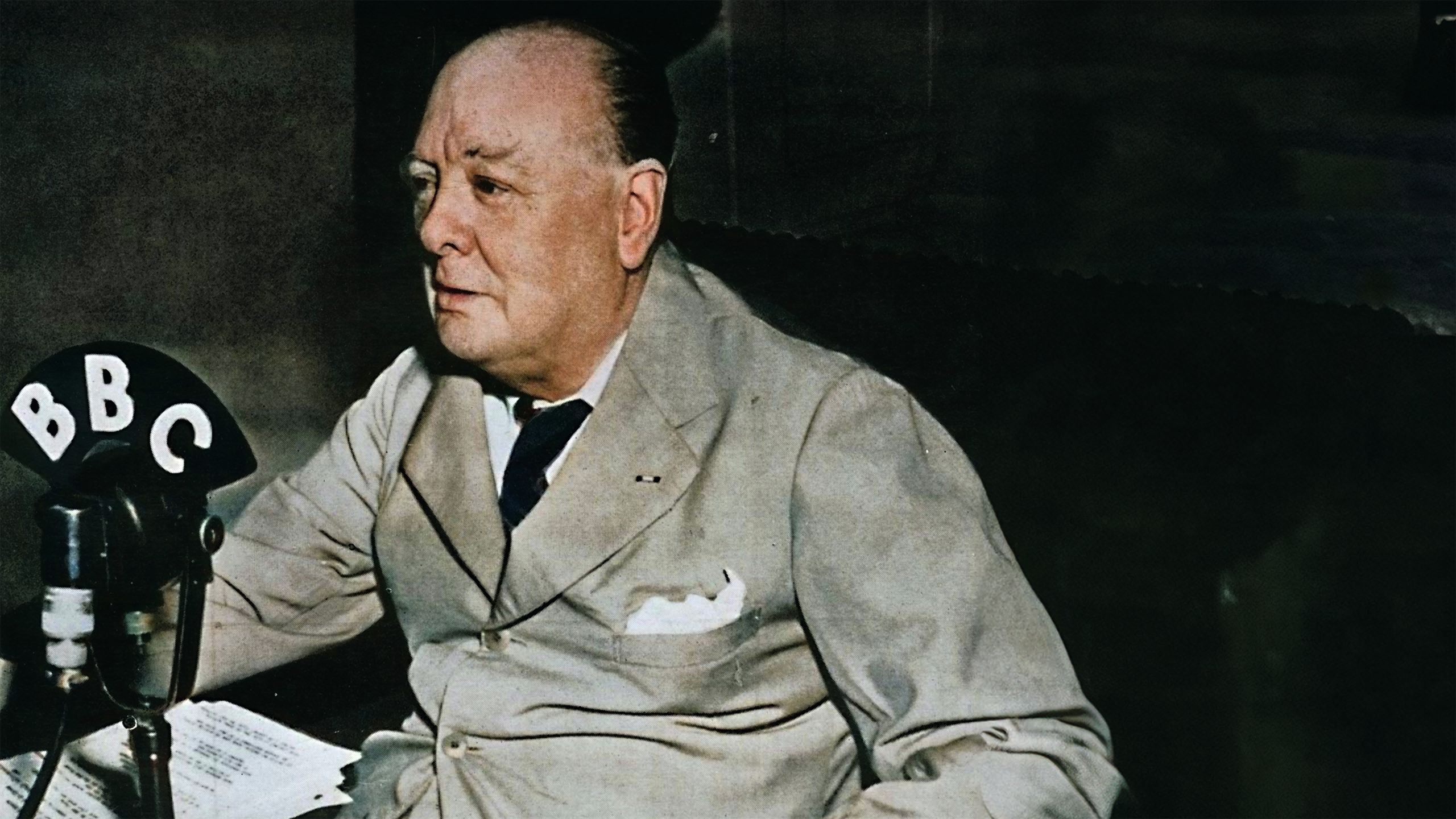 Colour photo of Churchill in a grey suit in front of a BBC microphone
