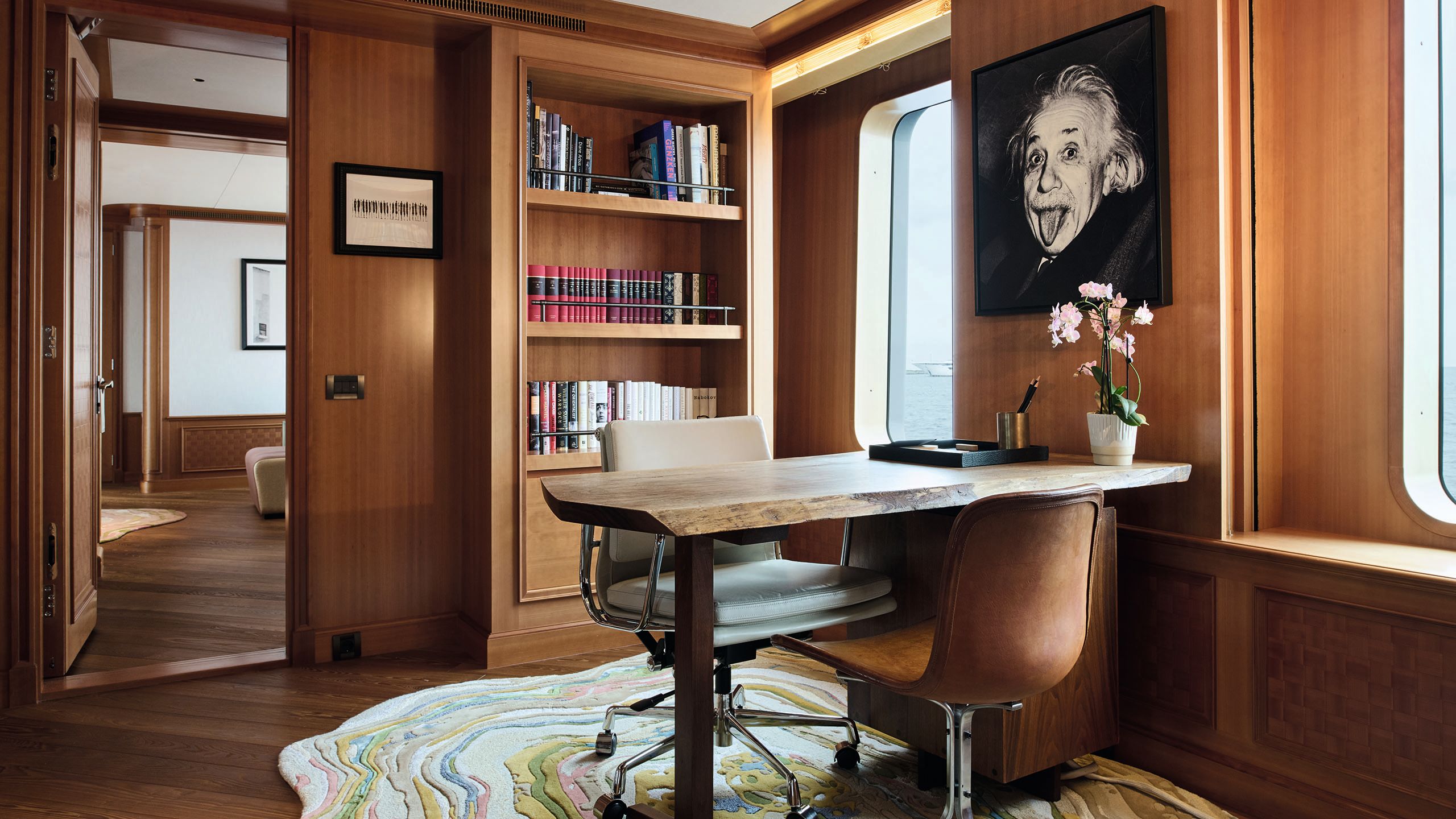 Office space with teak bookshelves and doors. There is a desk with two chairs facing each other and a black and white picture of Einstein sticking his tongue out on the wall