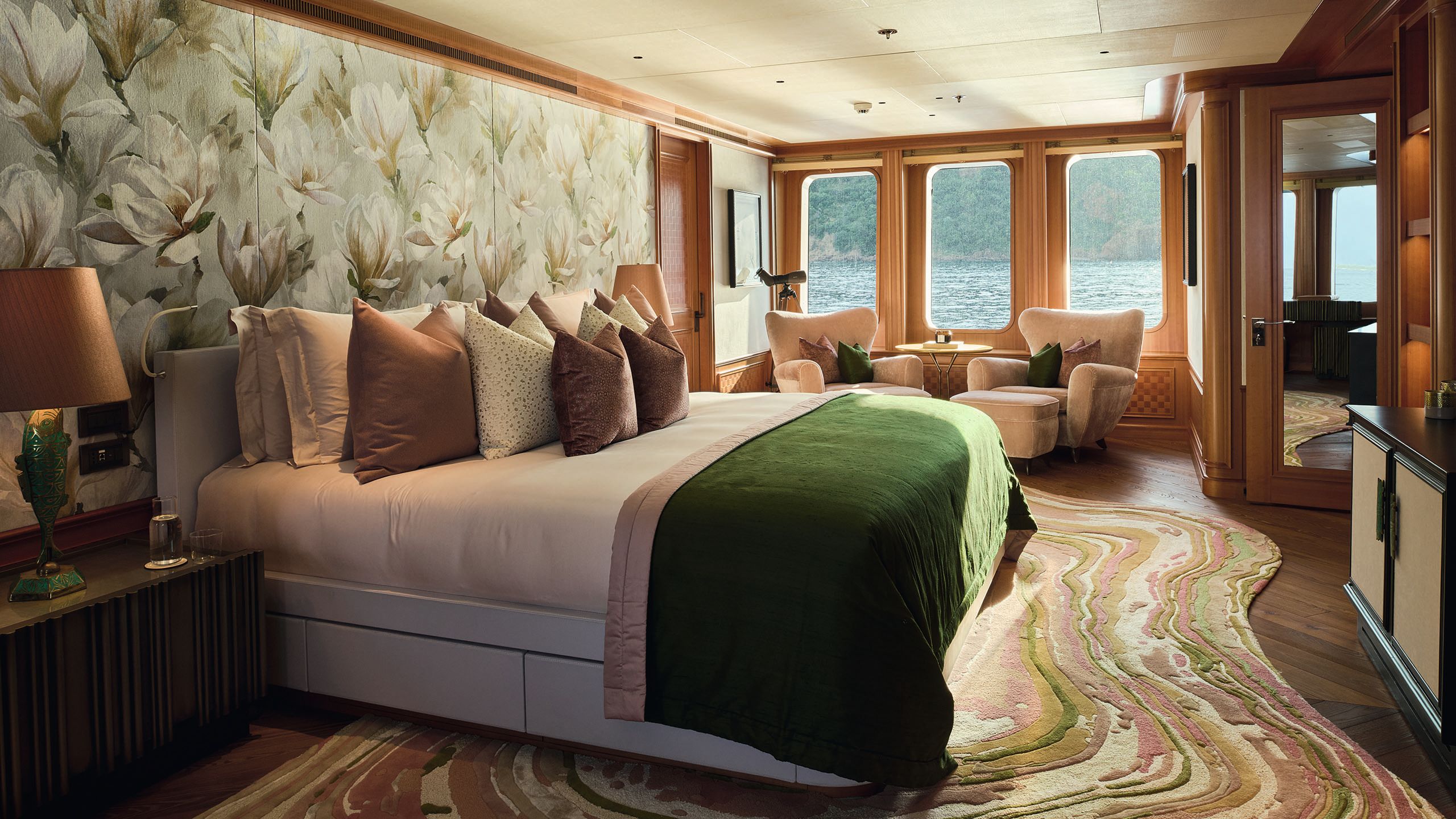 It now has abstract flower wallpaper behind the bed in a pale green and muted pink, which matches the bedding and throw cushions. Two pink chairs are in the window next to a gold telescope