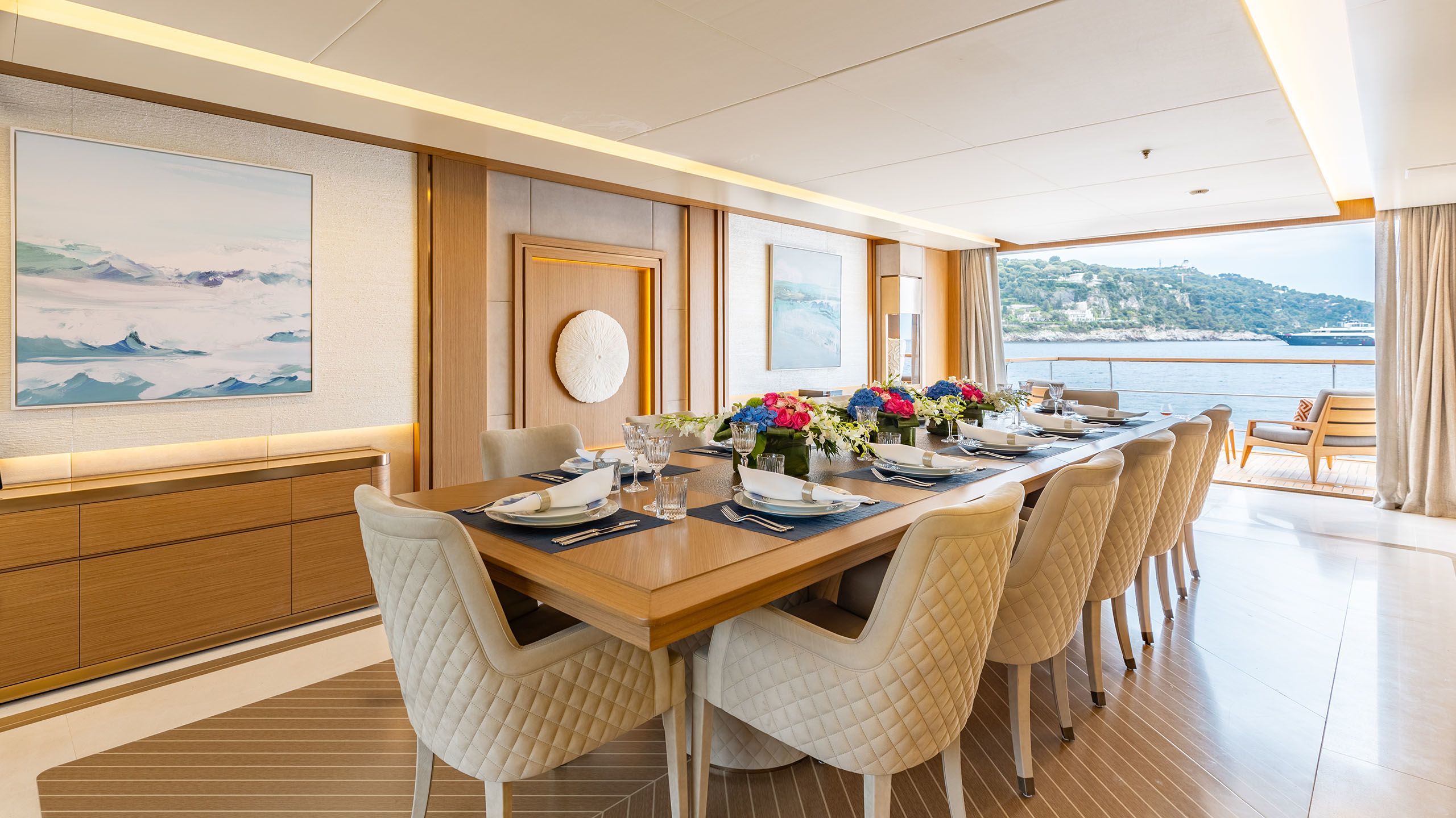 Interior of Alfa showing long dining table with seating for 10. Doors open on to the deck in the background