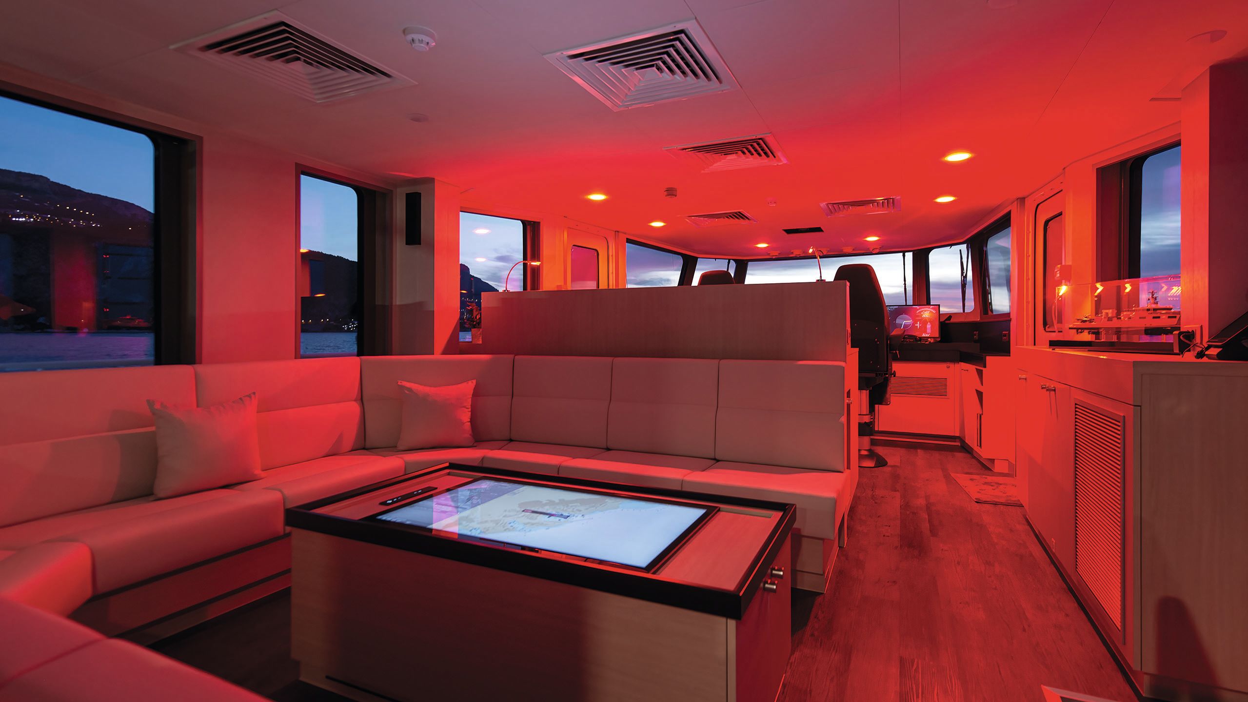 A touchscreen in the centre of a table with soft seats surrounding it. The room is lit up red