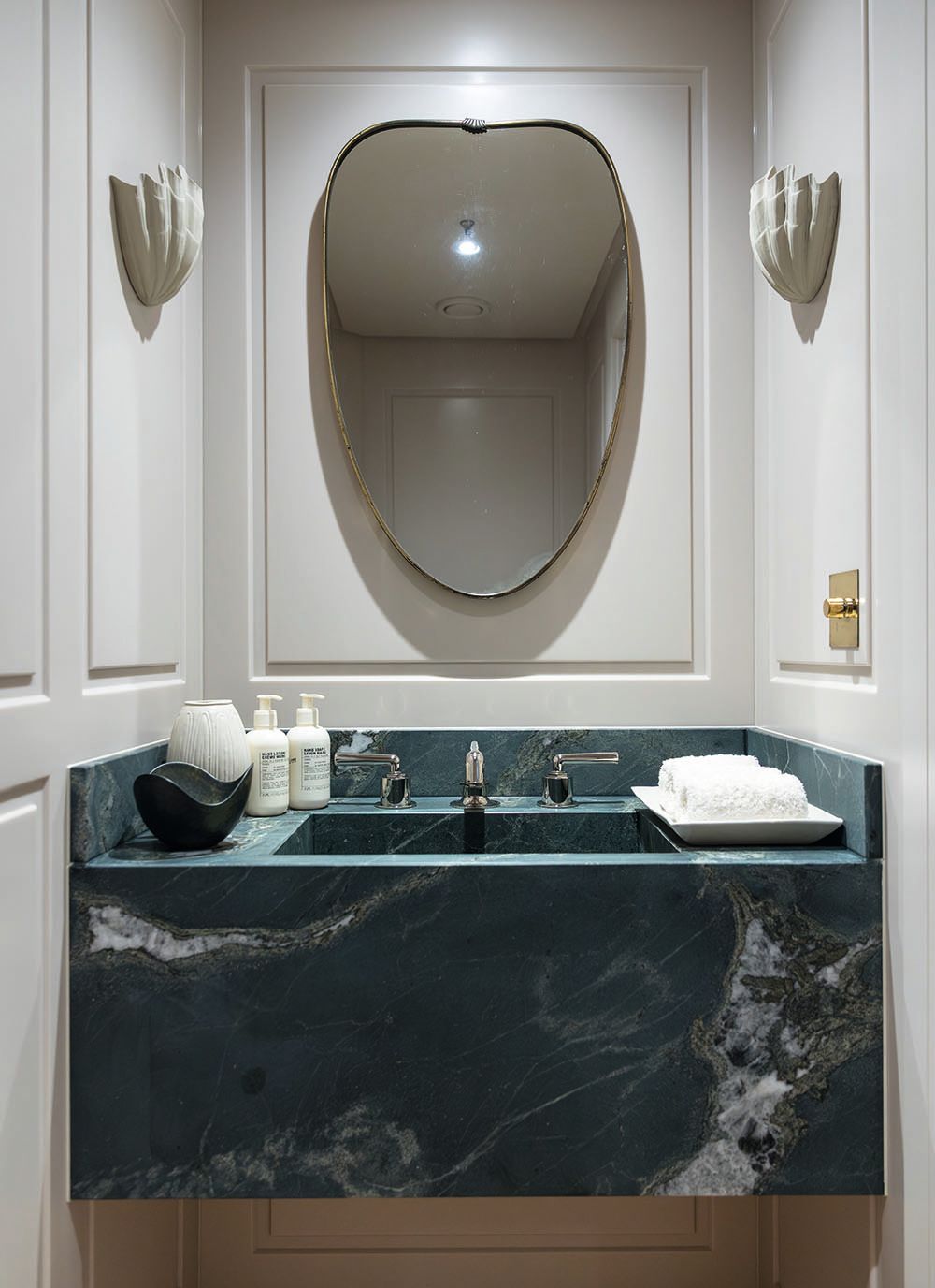 The marble surround in an en suite. There's a mirror above the sink, white flannels to the side and white scones on the white walls
