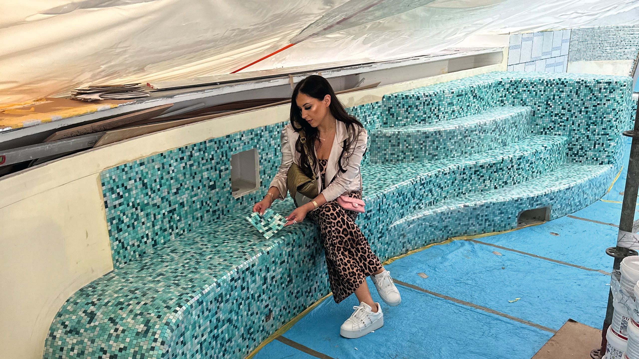 Khan looking at mosaic swatches. She is sitting on a ledge in the pool which is already tiled