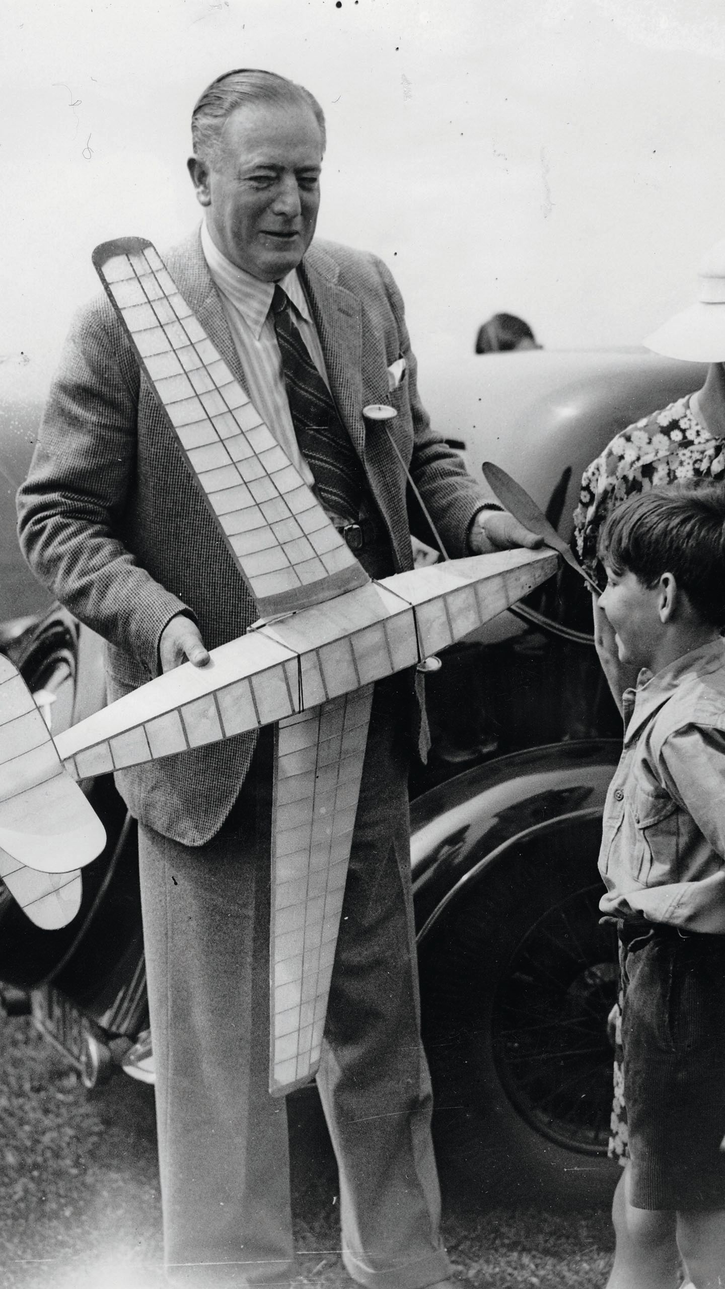 Black and white photo of Richard Fairey holding a model plane and showing it to a child