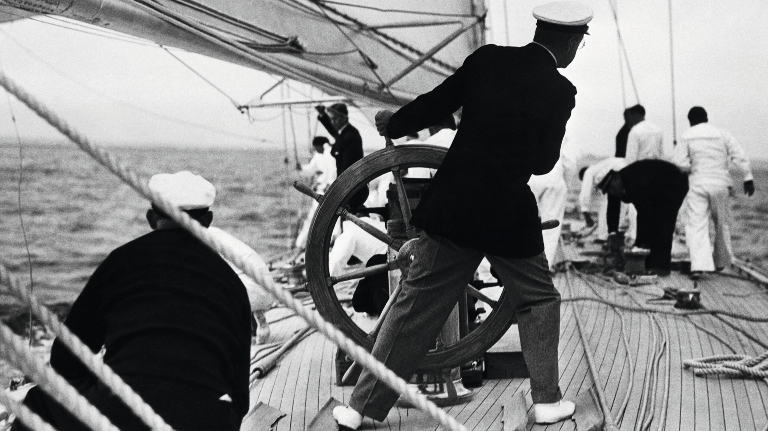 A black and white photo taken from behind of a man steering a vessel