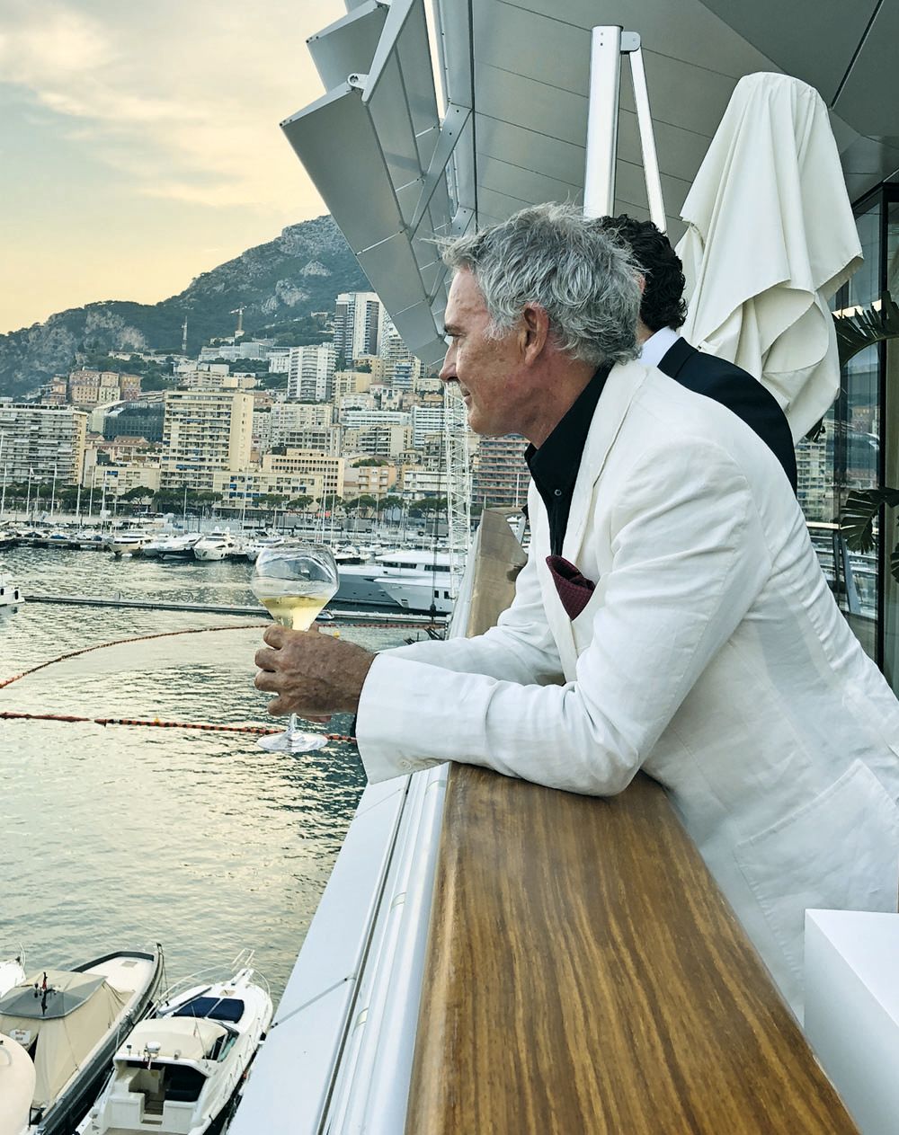 Steve Owen leaning over the side of a boat. He's wearing a white suit and holding a glass of white wine