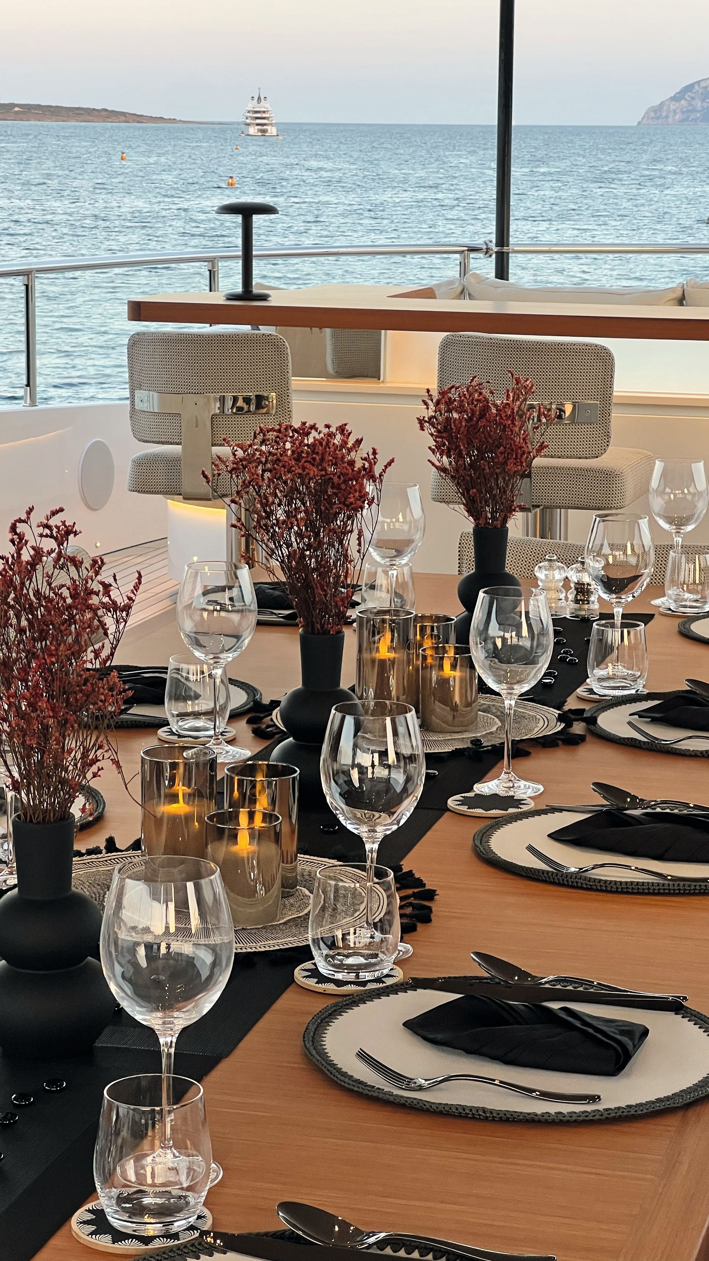 A set dining table on an outdoor deck - there are wine glasses, plates, cutlery and flowers on the table