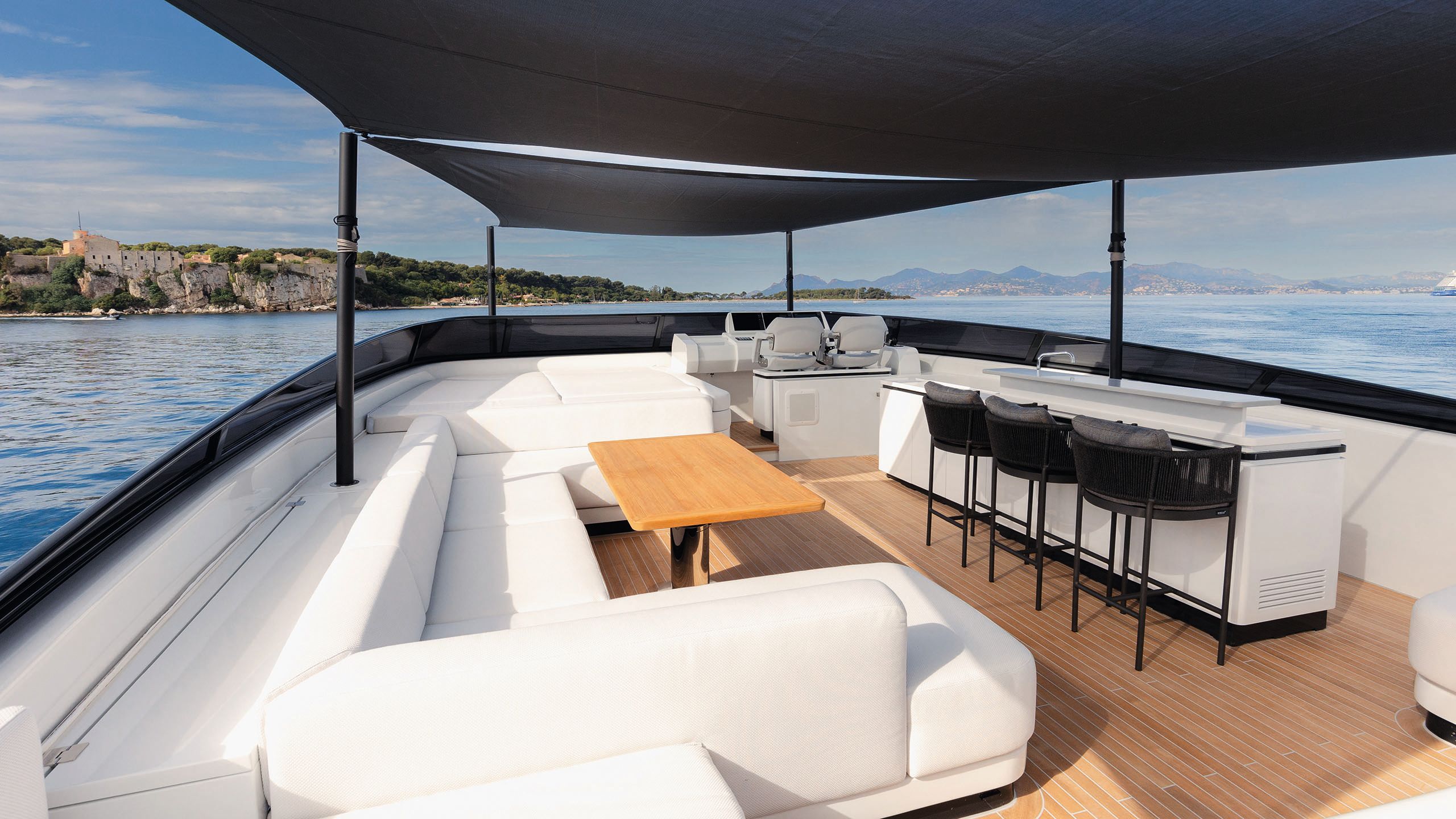 Covered outdoor area featuring large white sofa, brown table, and white bar area with tall black stools