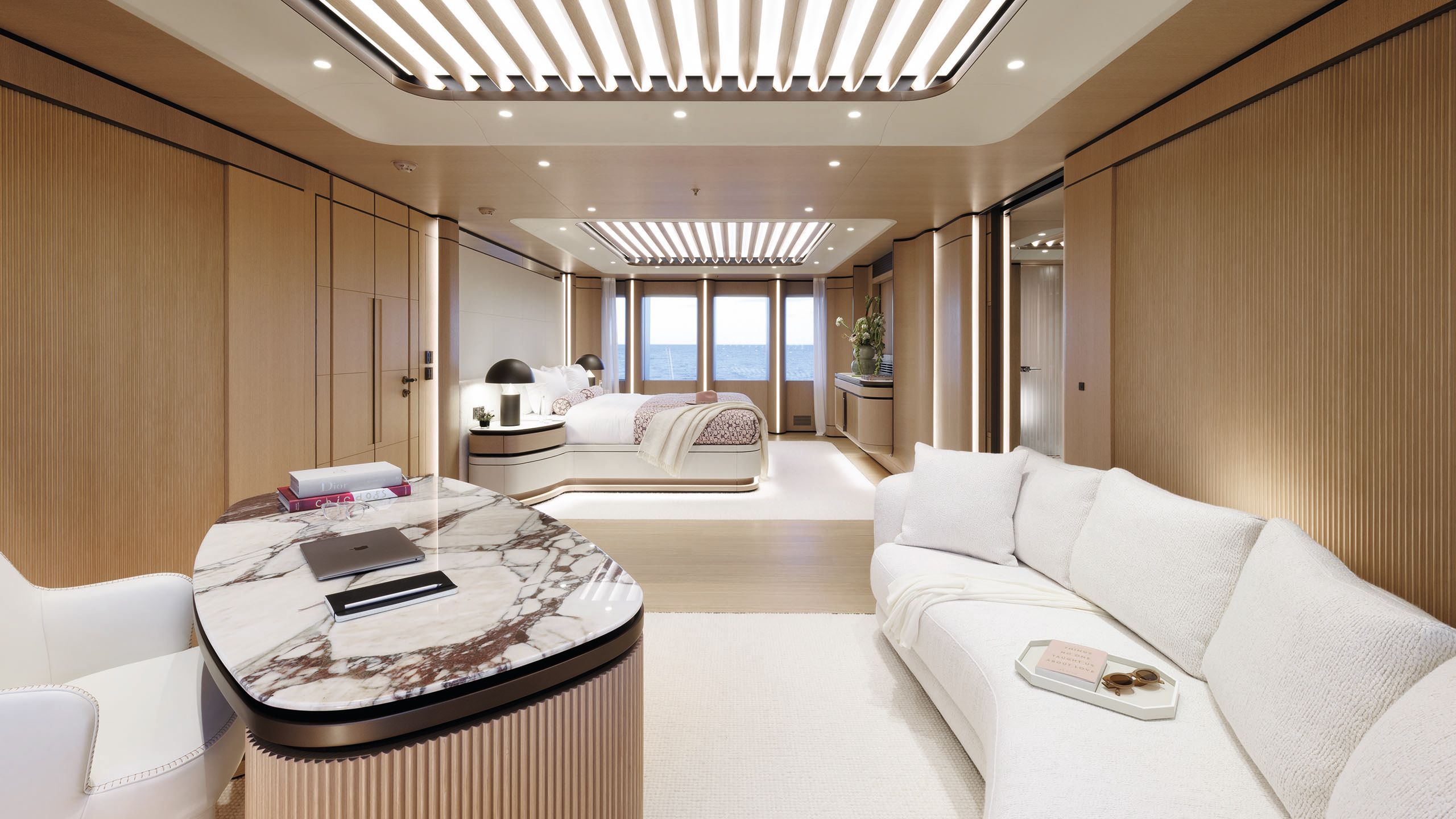 Long view of cabin - the bed is at the back and a marble topped desk and chair and white curved sofa are in the foreground