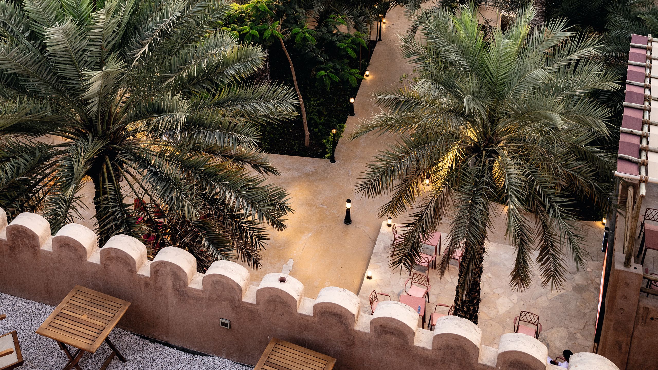View from a balcony looking down on to a square. The stone is a terracotta colour and there are palm trees