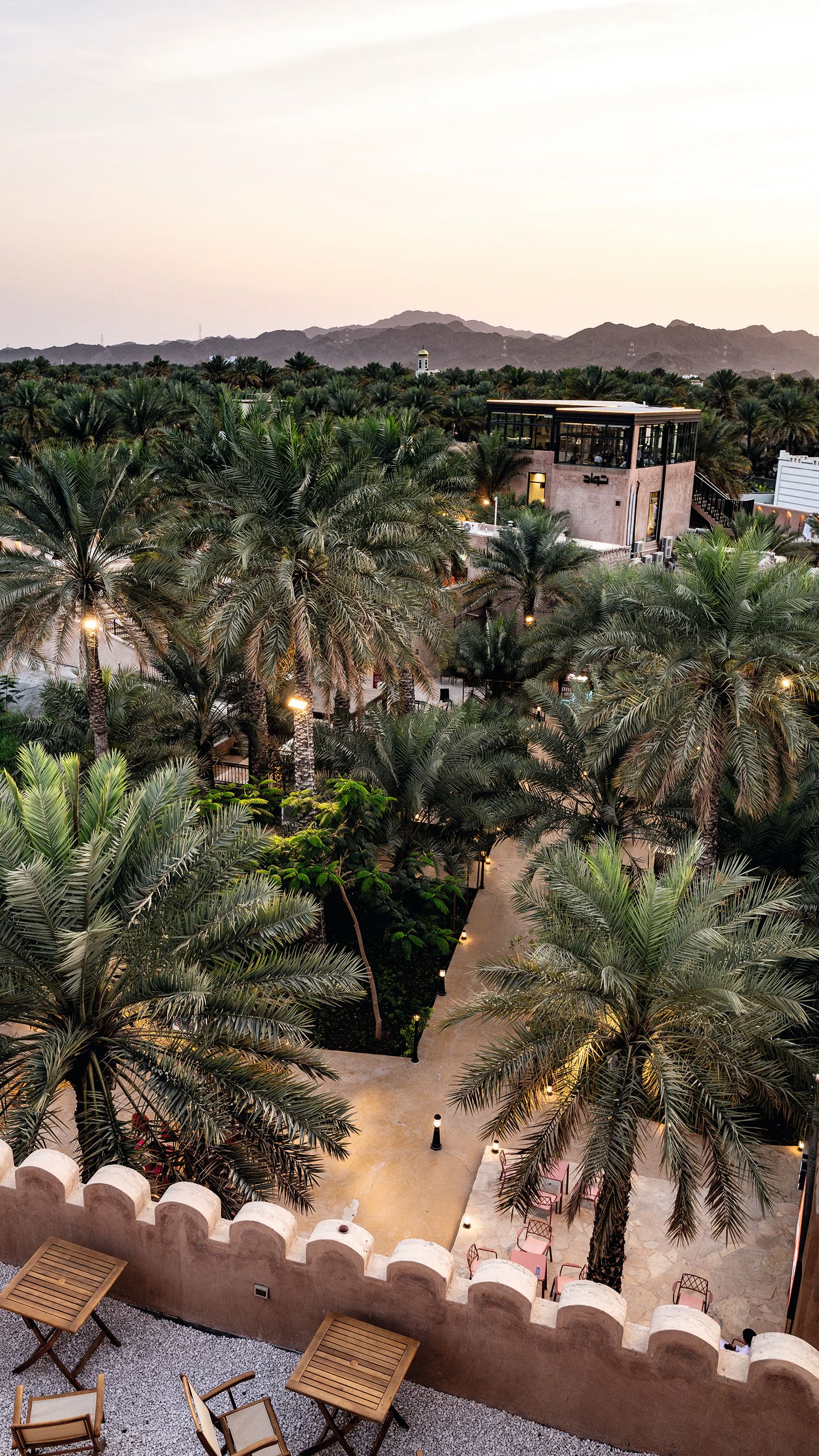 View from a balcony looking down on to a square. The stone is a terracotta colour and there are palm trees