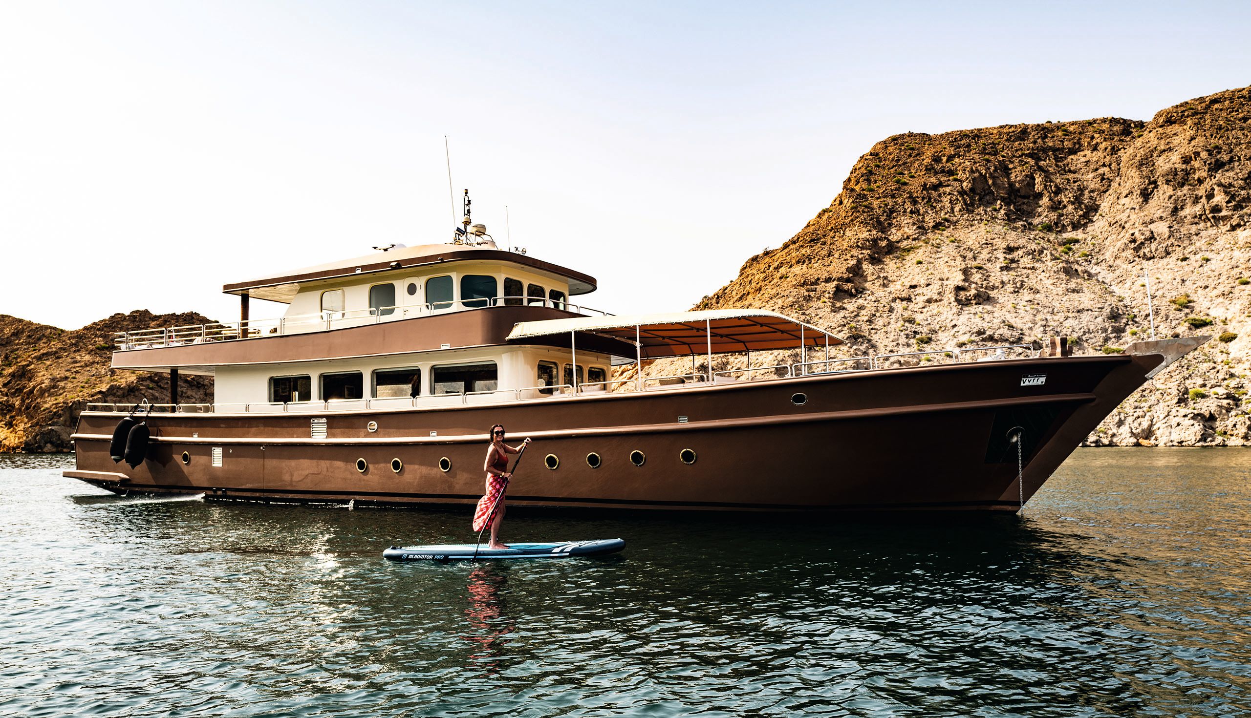 Ibra, a modern reincarnation of the traditional dhow. A woman is on a paddle board in front of the boat and looking at the camera