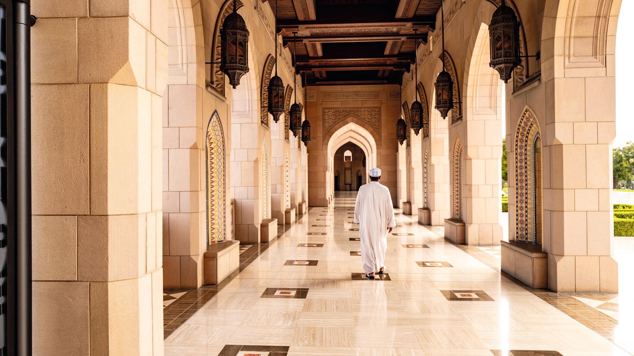 View from behind of a man walking down a marbled hallway in a mosque