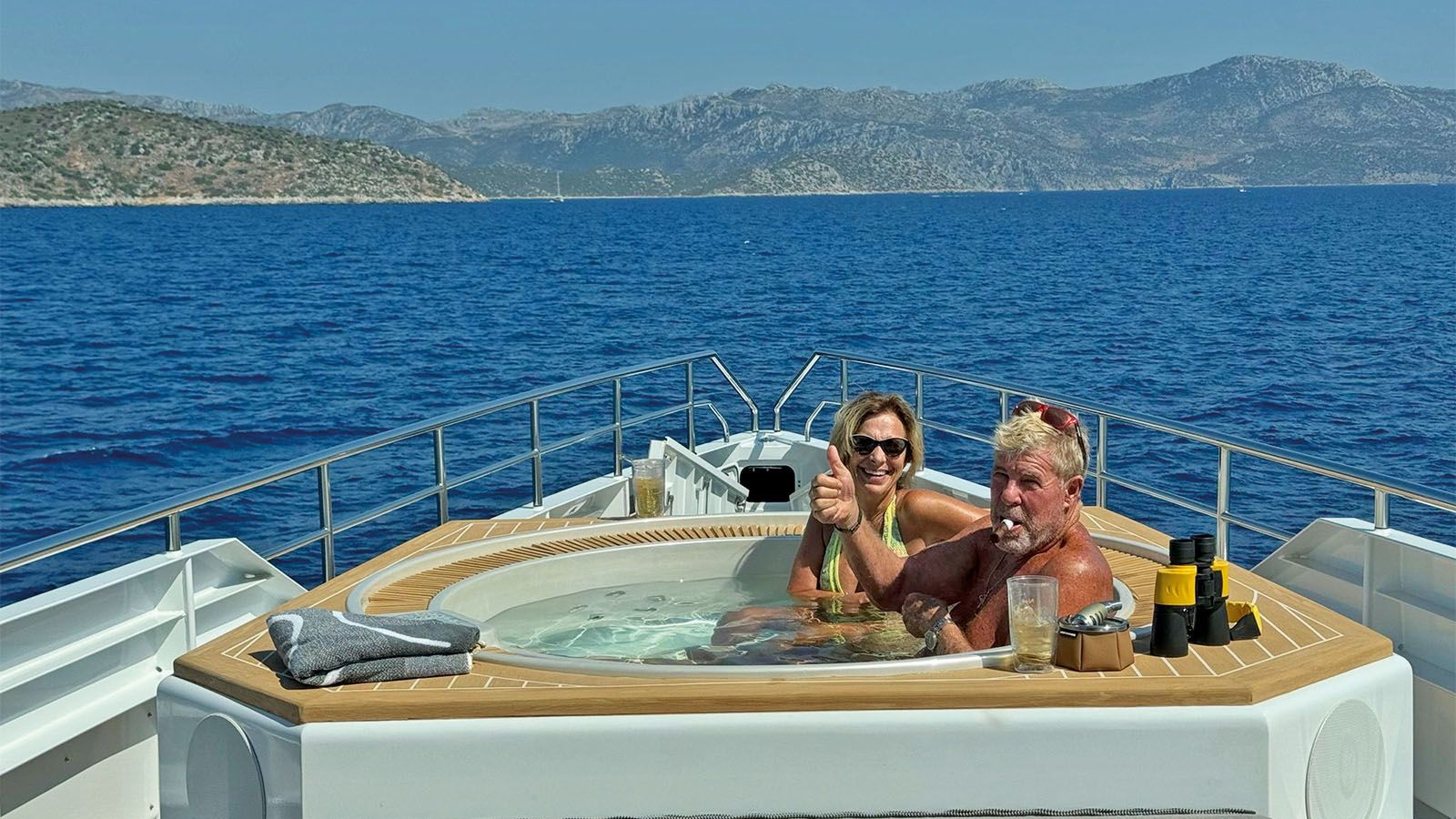 Minea and his wife Becky sitting in a hot tub. He is doing a thumbs up and has a cigar in his mouth.
