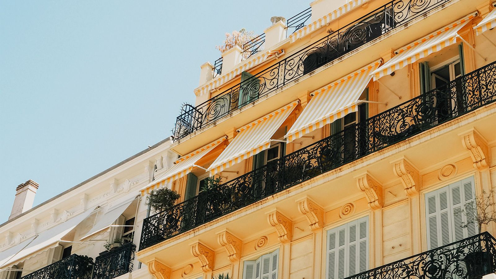 Yellow facades of houses in Cannes. They have black iron balconies and yellow and white striped awnings