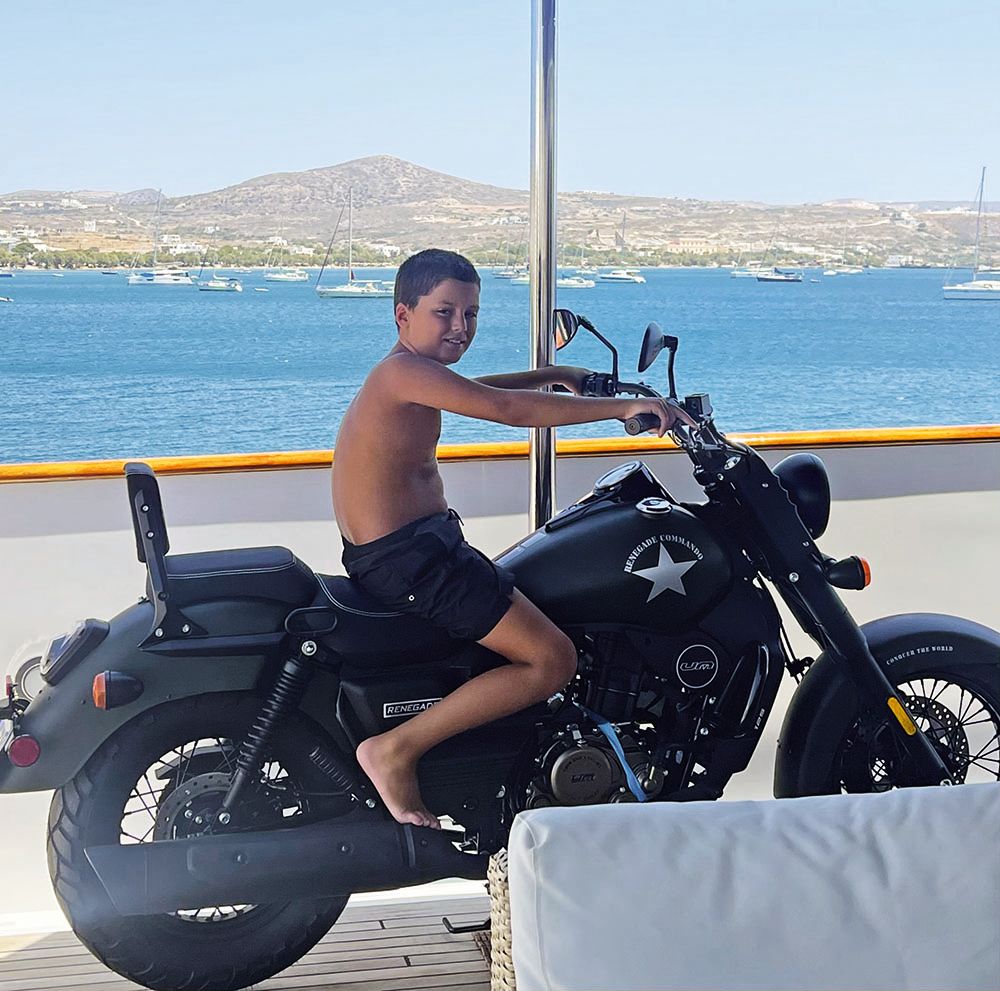 A young boy wearing dark shorts, sitting astride a motorbike