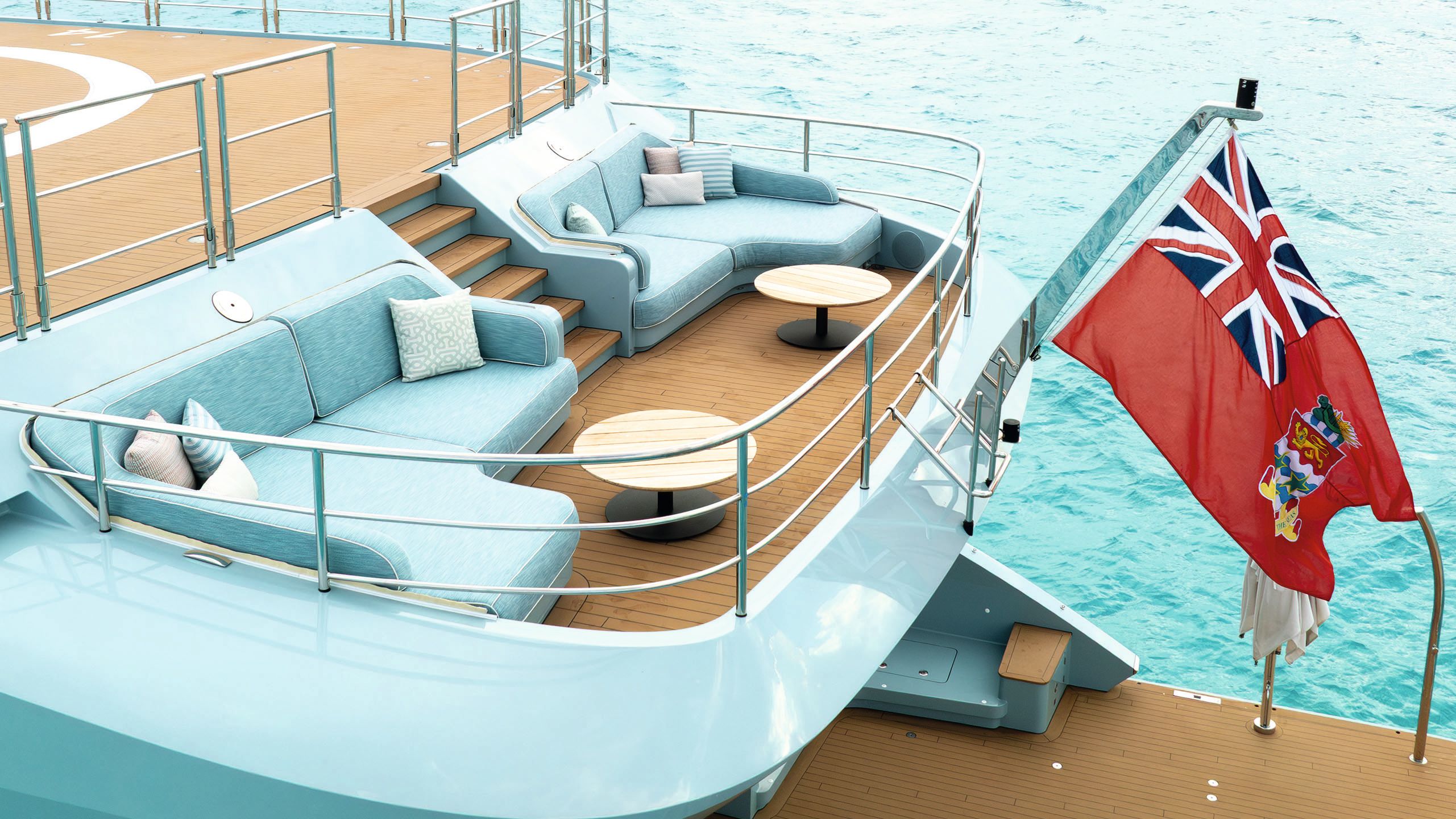 A balcony with a curved turquoise sofa in each corner. A red ensign flag is flying from a pole