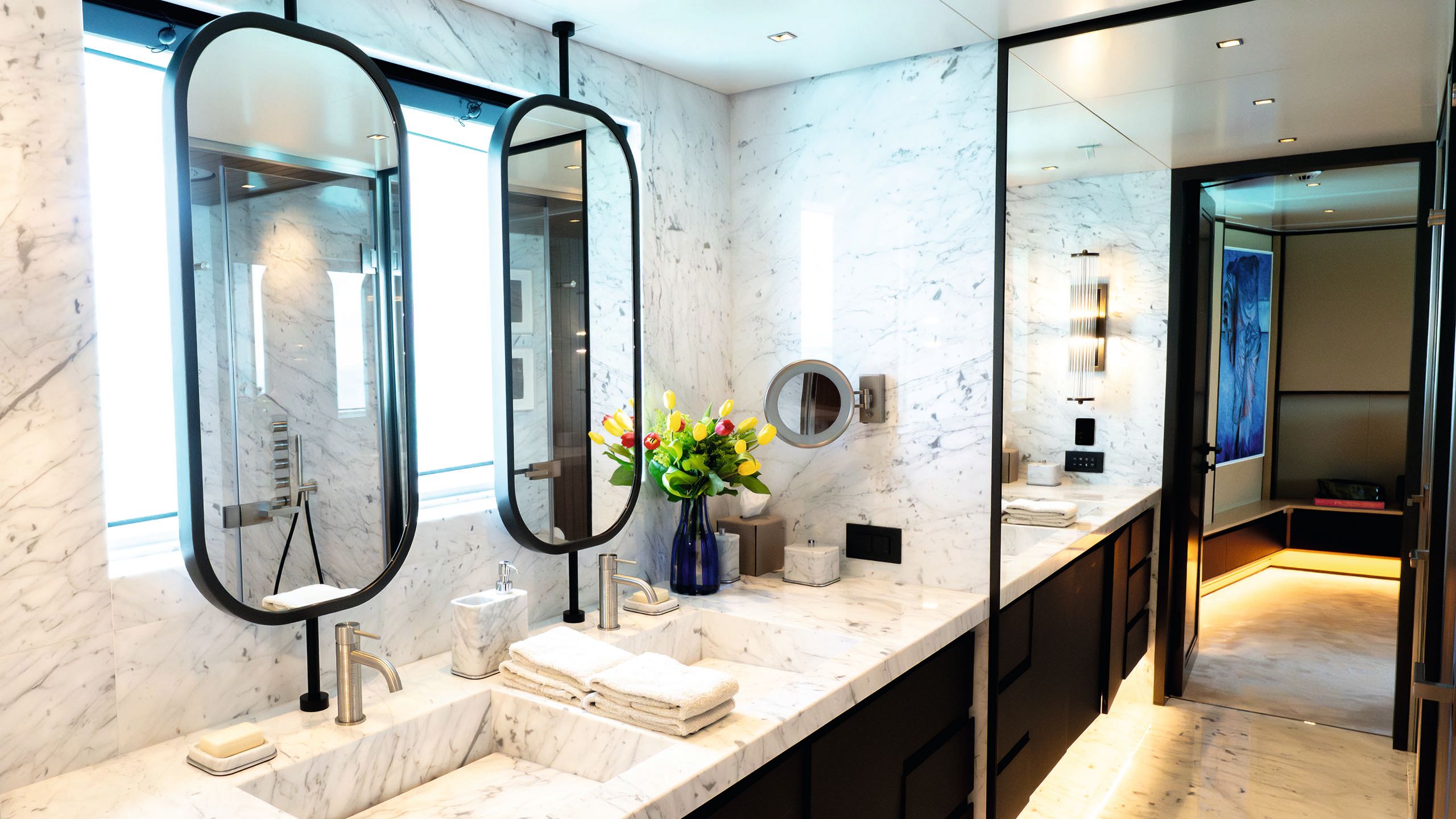 Inside the bathroom which has a double vanity with marble sinks and black mirrors