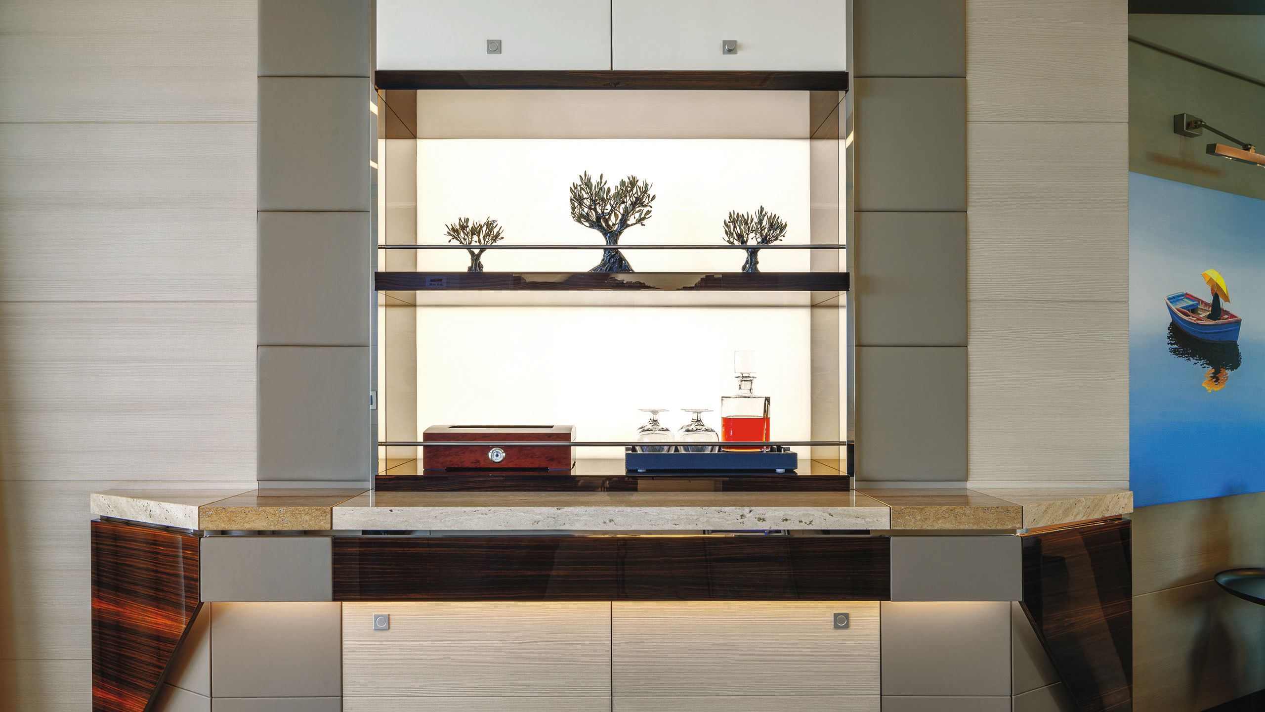 Neutral cupboards with backlit shelving that has black tree ornaments and drinks on