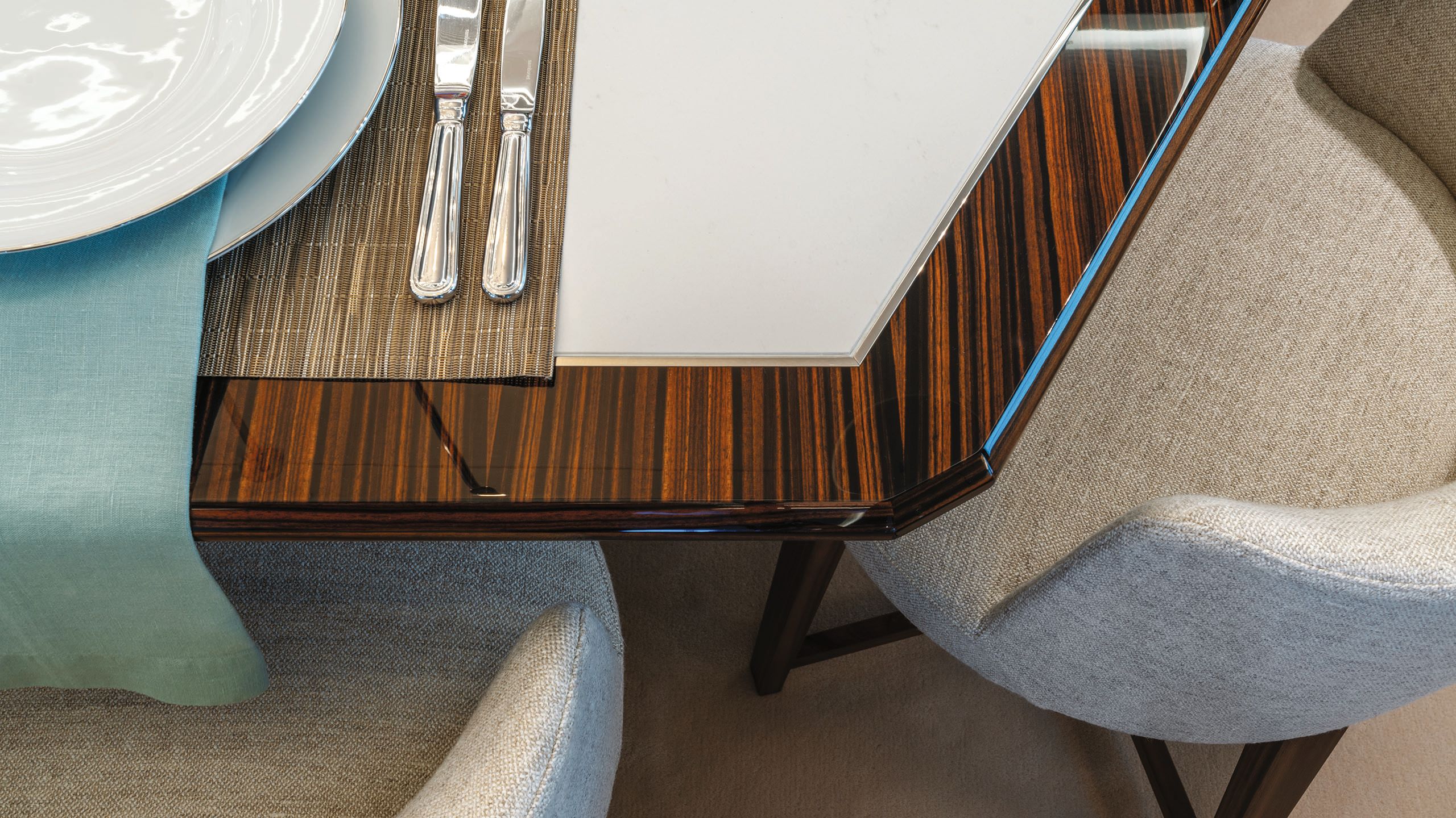 Overhead shot of the table which has a white inlay and mahogany surround. Also shows the edge of a grey chair and place settings with blue napkin