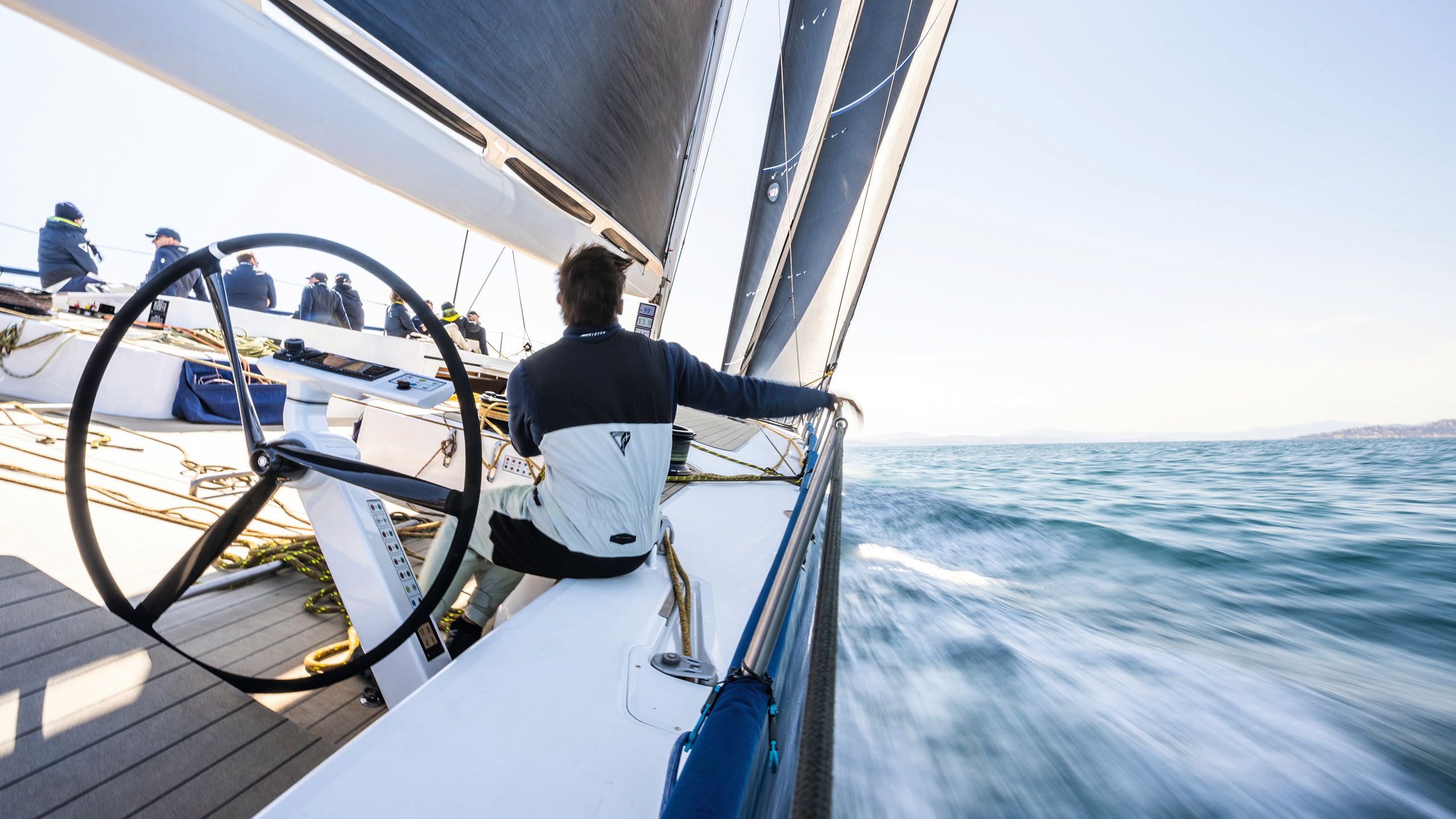 View from on board, looking down the deck. The vessel is tilting to the side on the water and a man has his back to the camera in the foreground