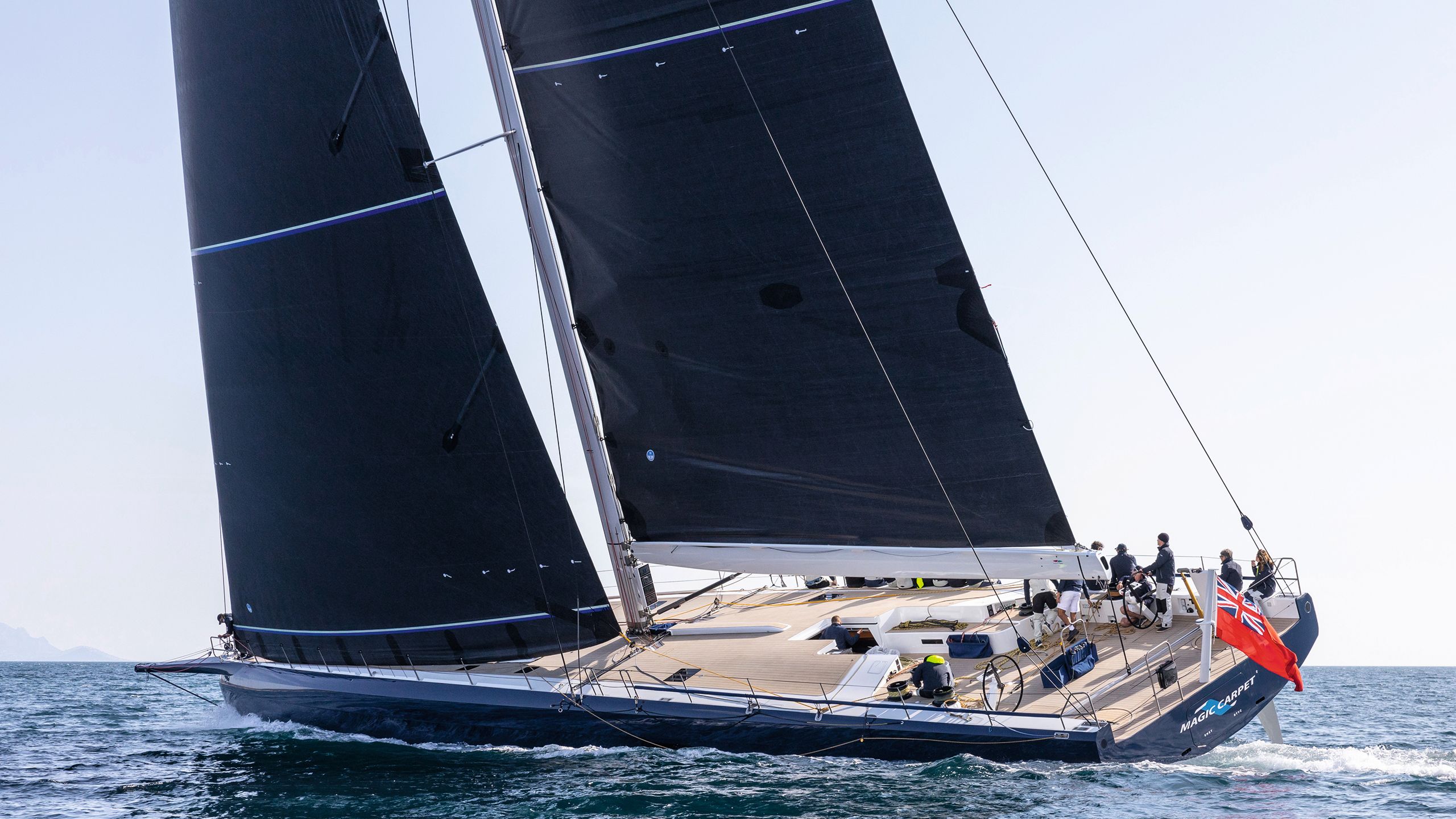 Side view of Magic Carpet E on the water with two dark sails up
