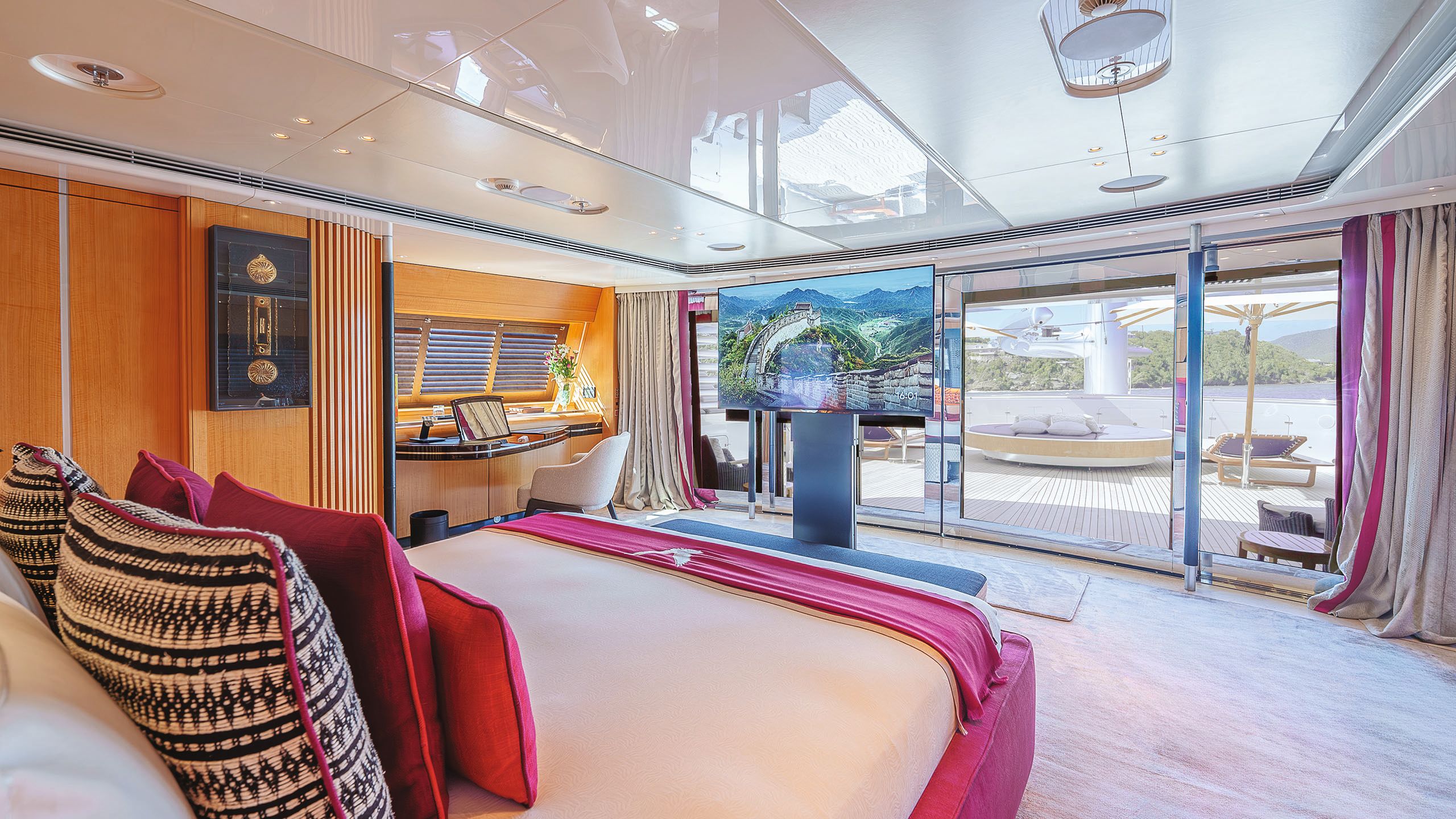 View of the VIP cabin looking out at the deck. The bed has white linens and pink, black and white cushions and throw