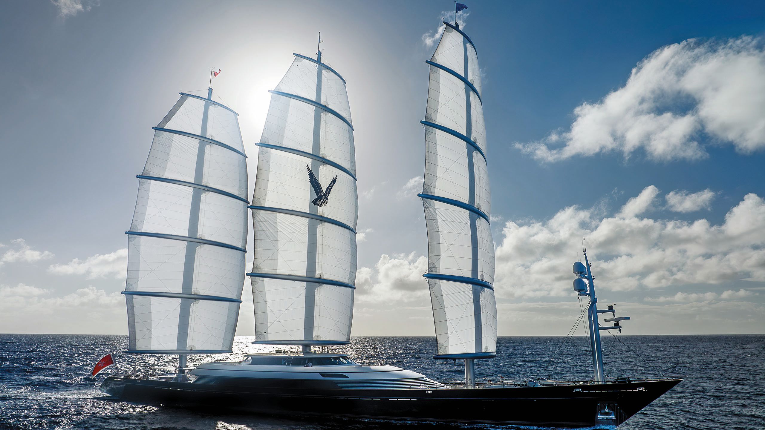 Wide shot of Maltese Falcon on the water, taken from the side. The sunlight is shining through its three sails