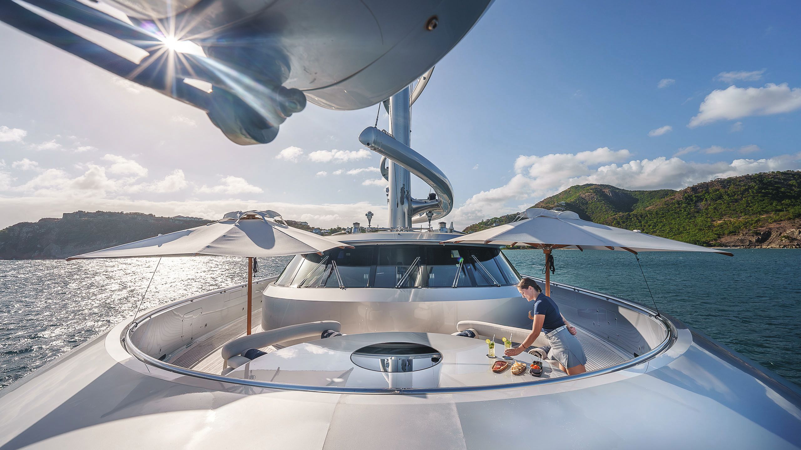 Two large parasols on an outdoor part of the deck. A woman is putting drinks on a circular table