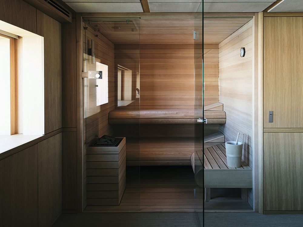Looking into the sauna, which has two levels and is finished with light wood and a glass door