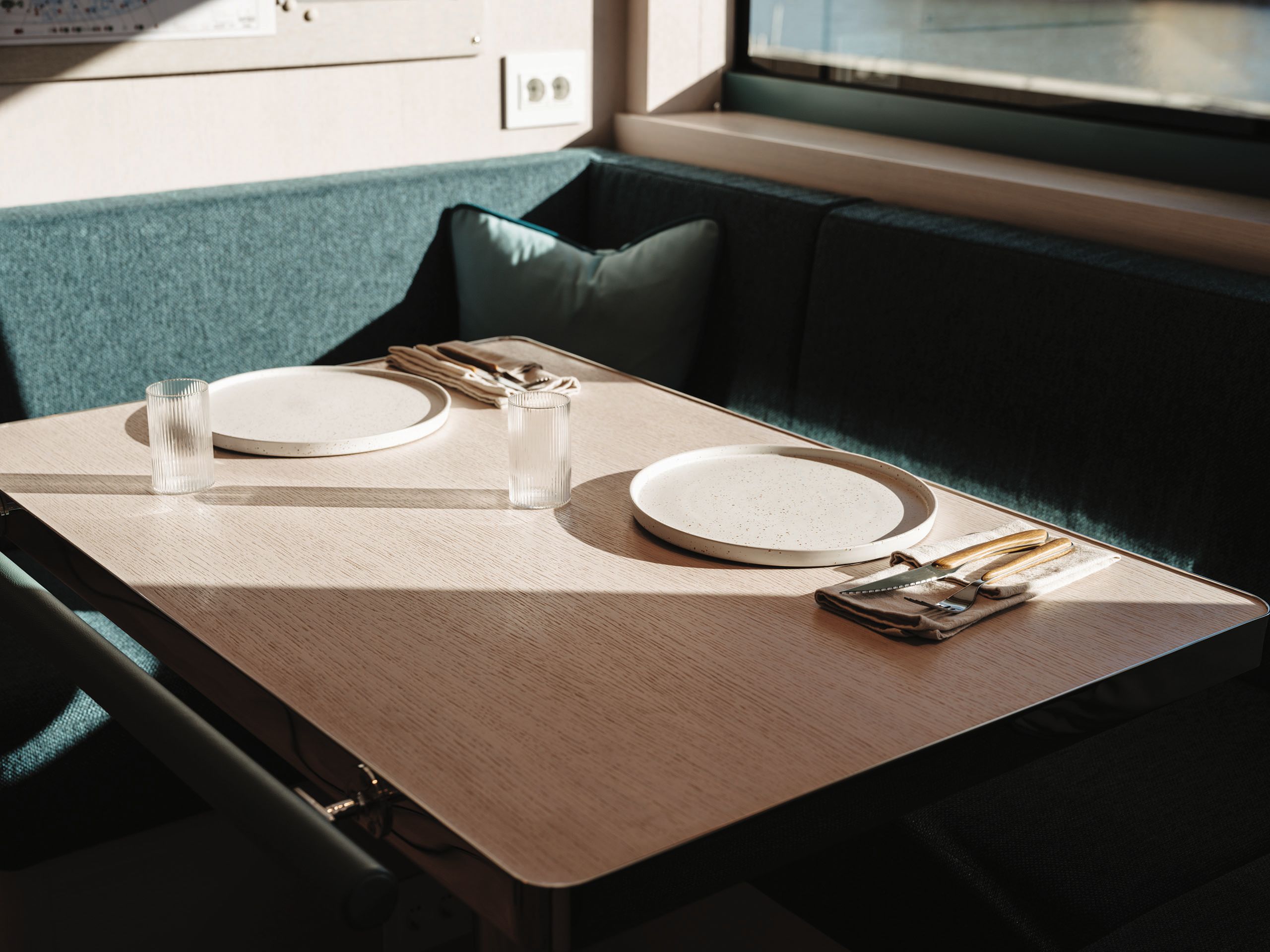 Corner seating in teal around a whitewashed oak dining table with settings for two