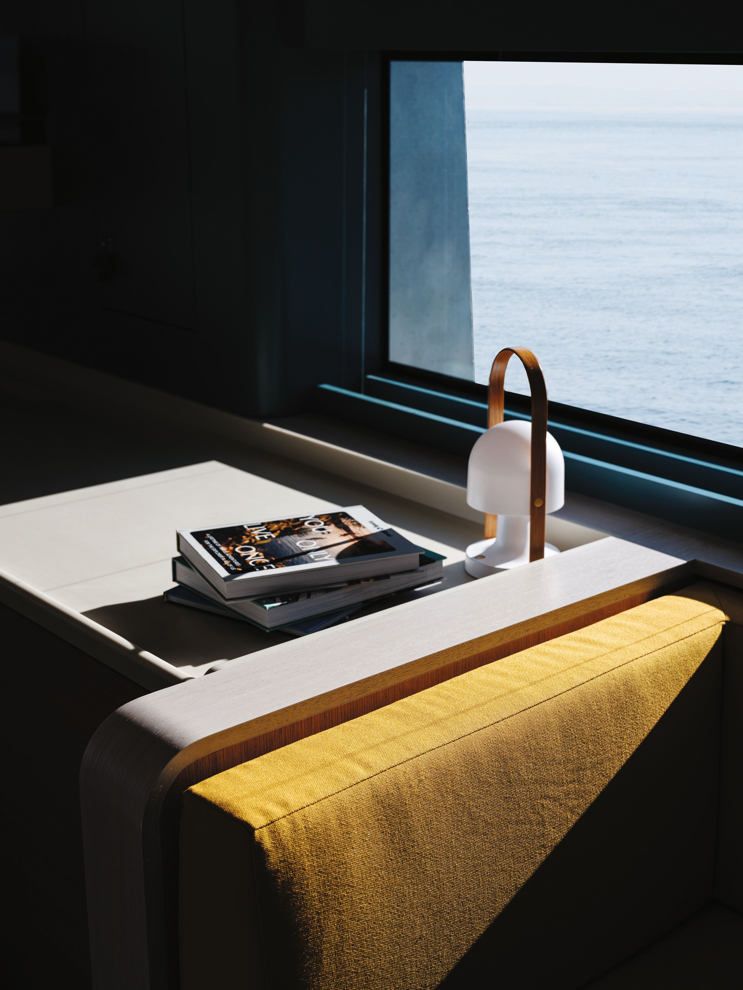 A table and white lamp with a handle. A yellow cushion is next to the table and there are books on top of it