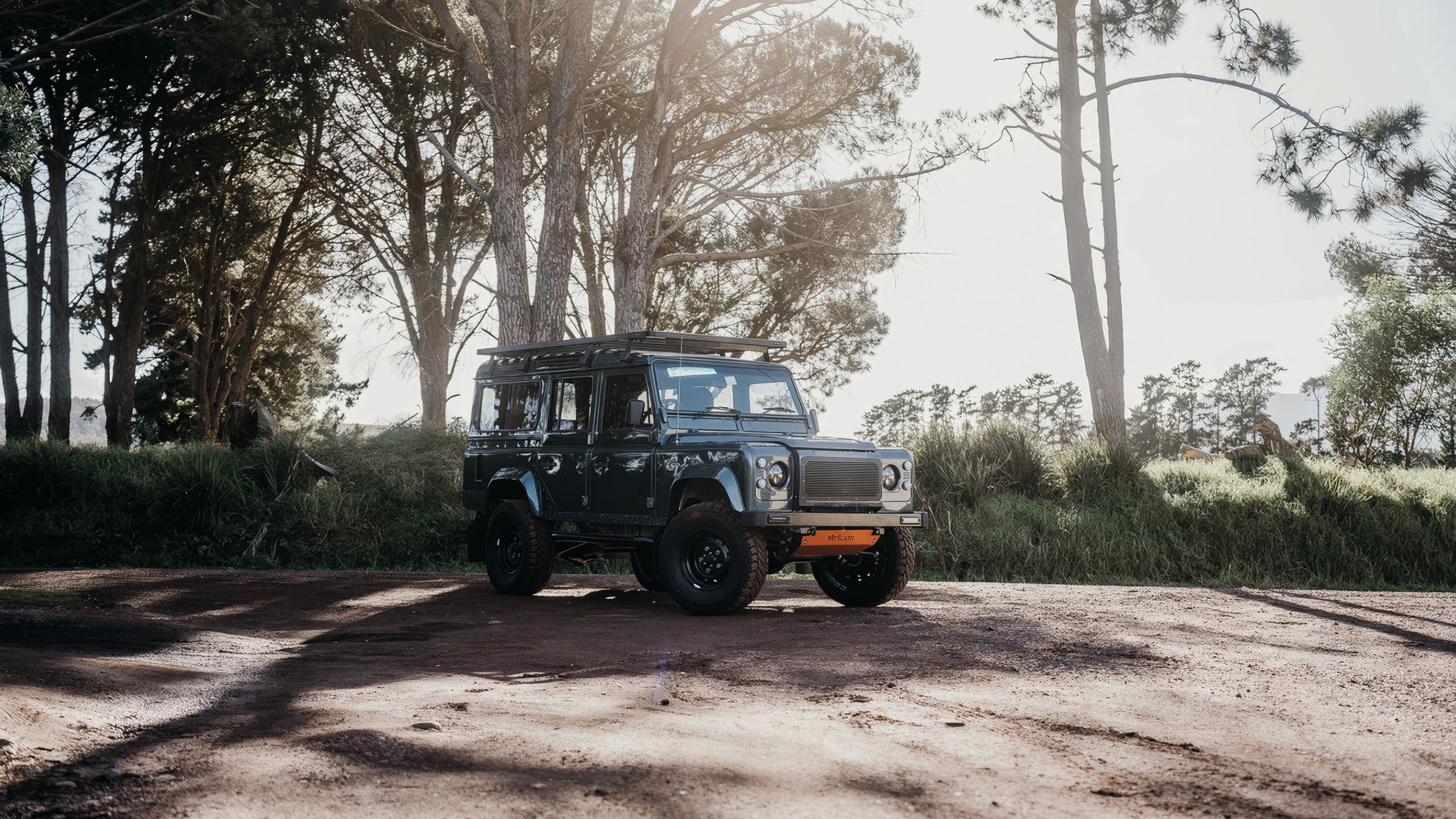 Jeep-style car in black on a dirt track with trees in the background
