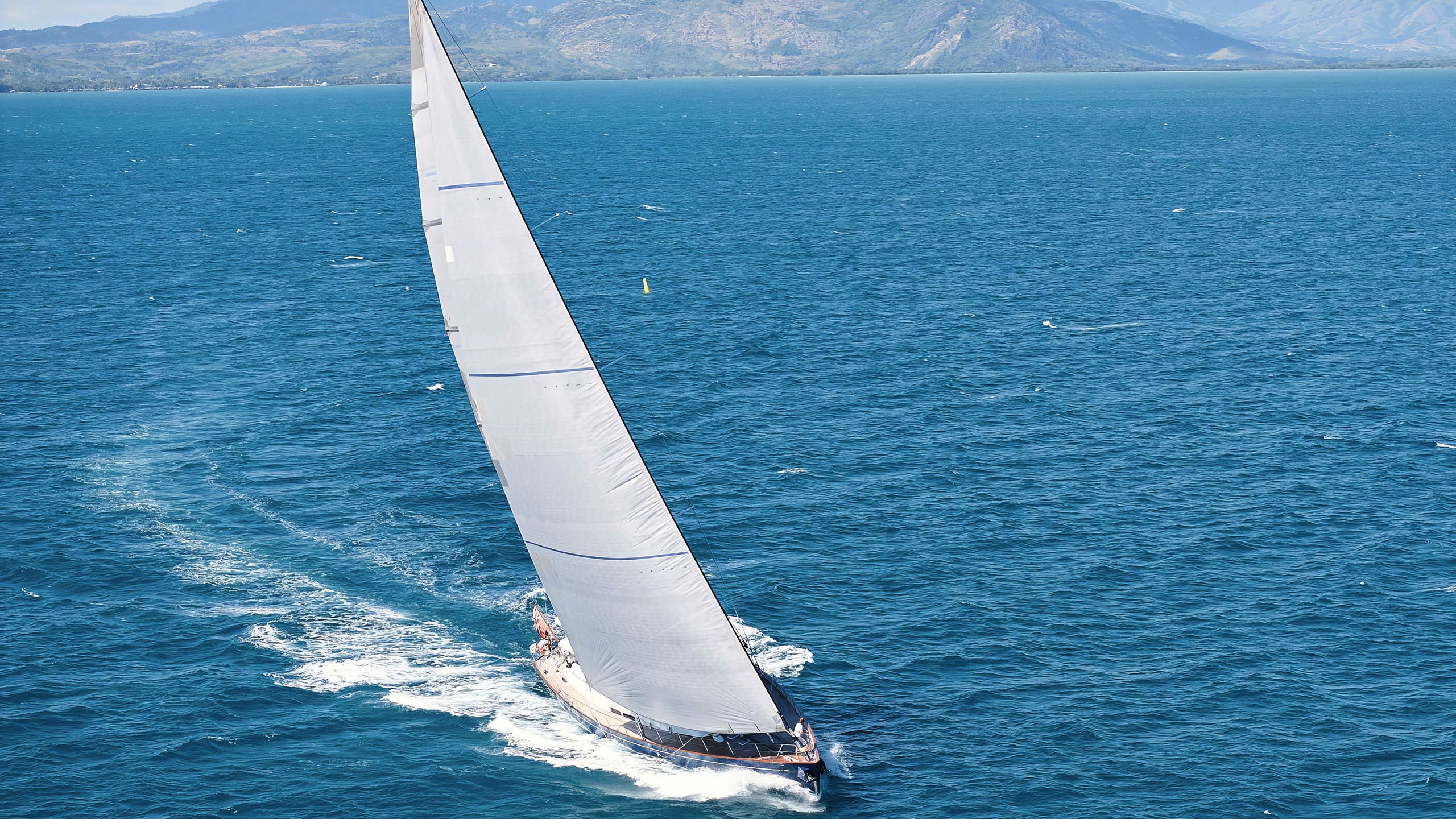 A faraway aerial shot of Kawil on the water. Its large white sail is up.