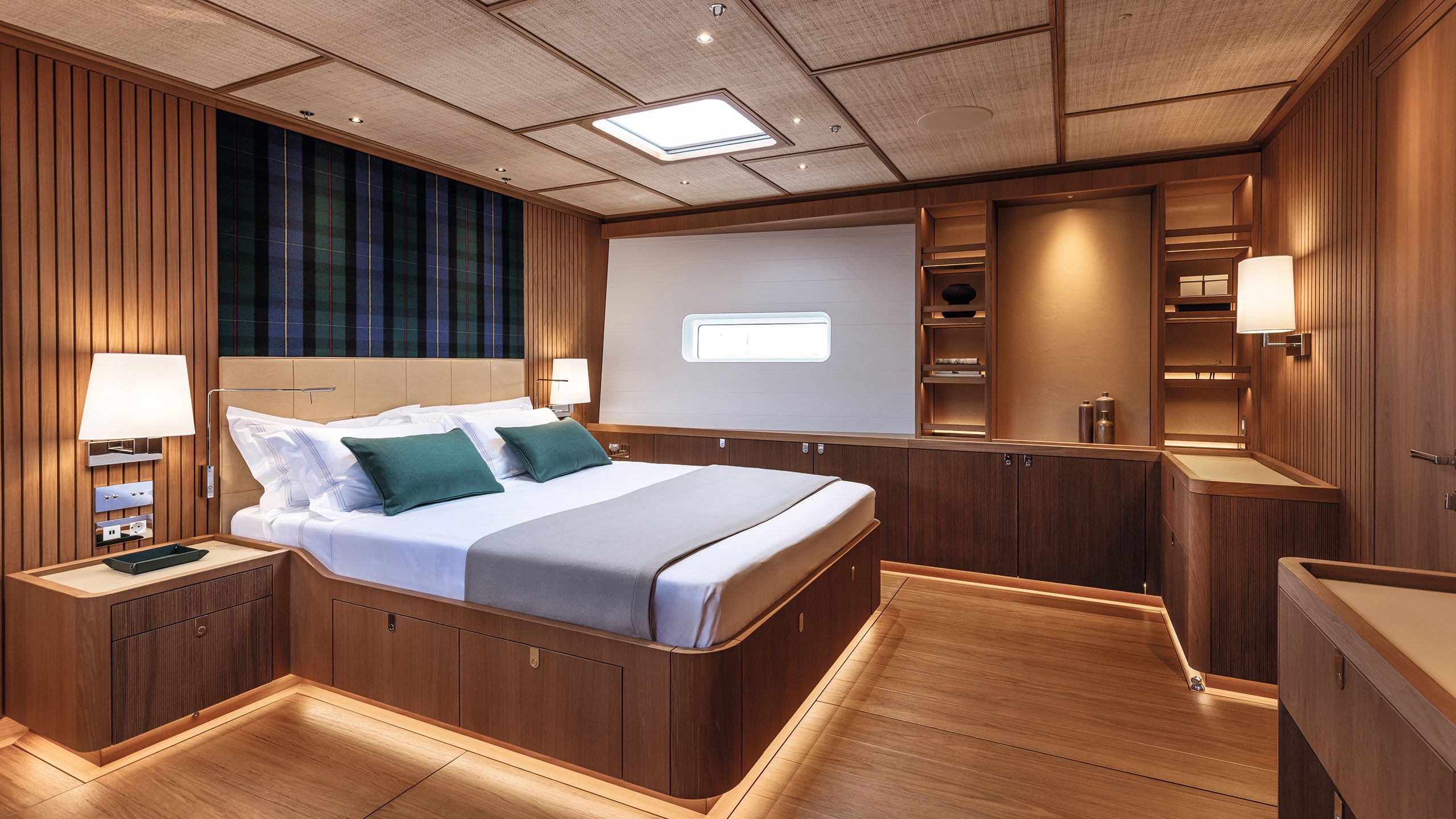 Large bed in the centre of the room with white sheets, grey throw and green cushions. The headboard has blue and green tartan material. The room has a wooden floor and wood panneling on the walls