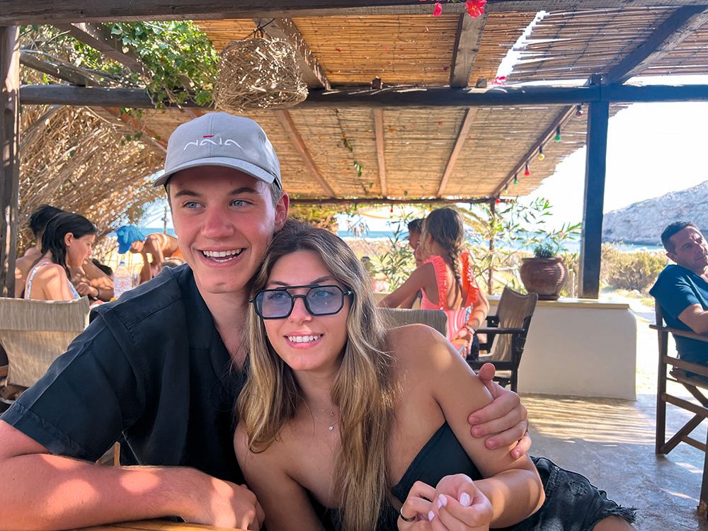 Aimillia has long light brown hair and is wearing blue-tinted sunglasses. Her boyfriend is wearing a dark top and light blue cap