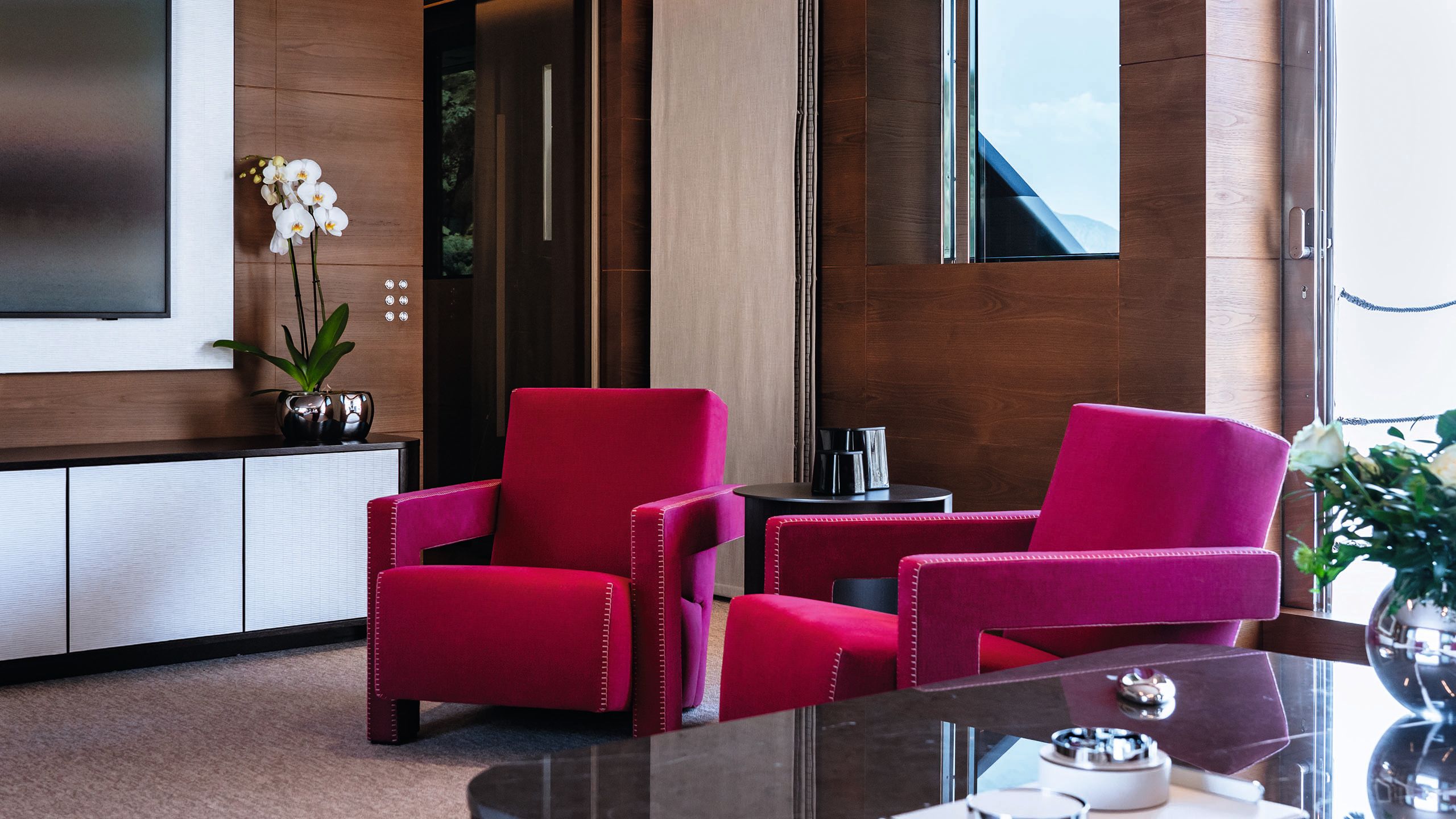 Two deep red armchairs with a tv and cabinet to the left and table to the right