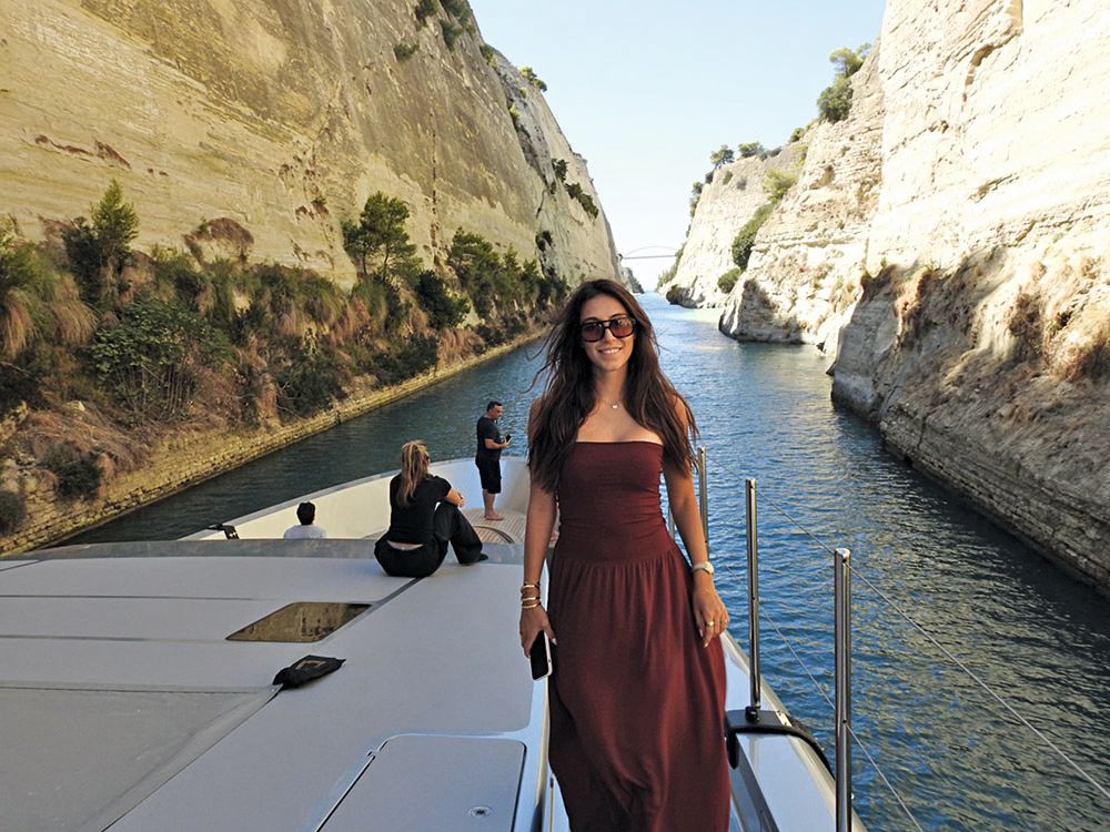 Natalia has long brown hair and is wearing a burgandy dress and large brown sunglasses