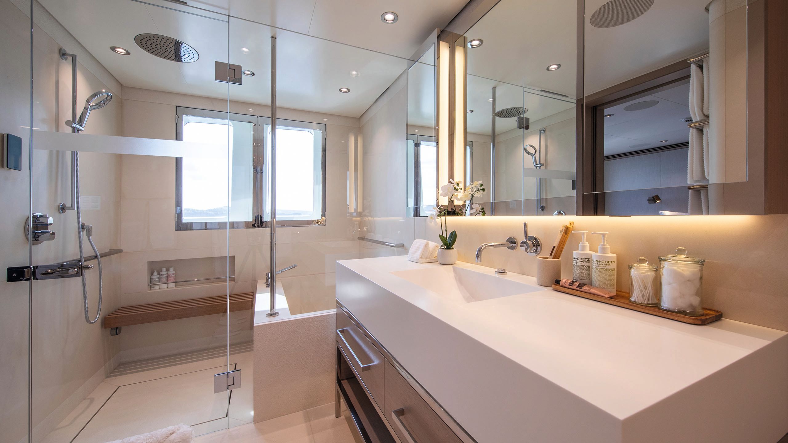 View of a bathroom with glass shower and bath cubicle at one end. It's done in neutral colours and chrome fittings