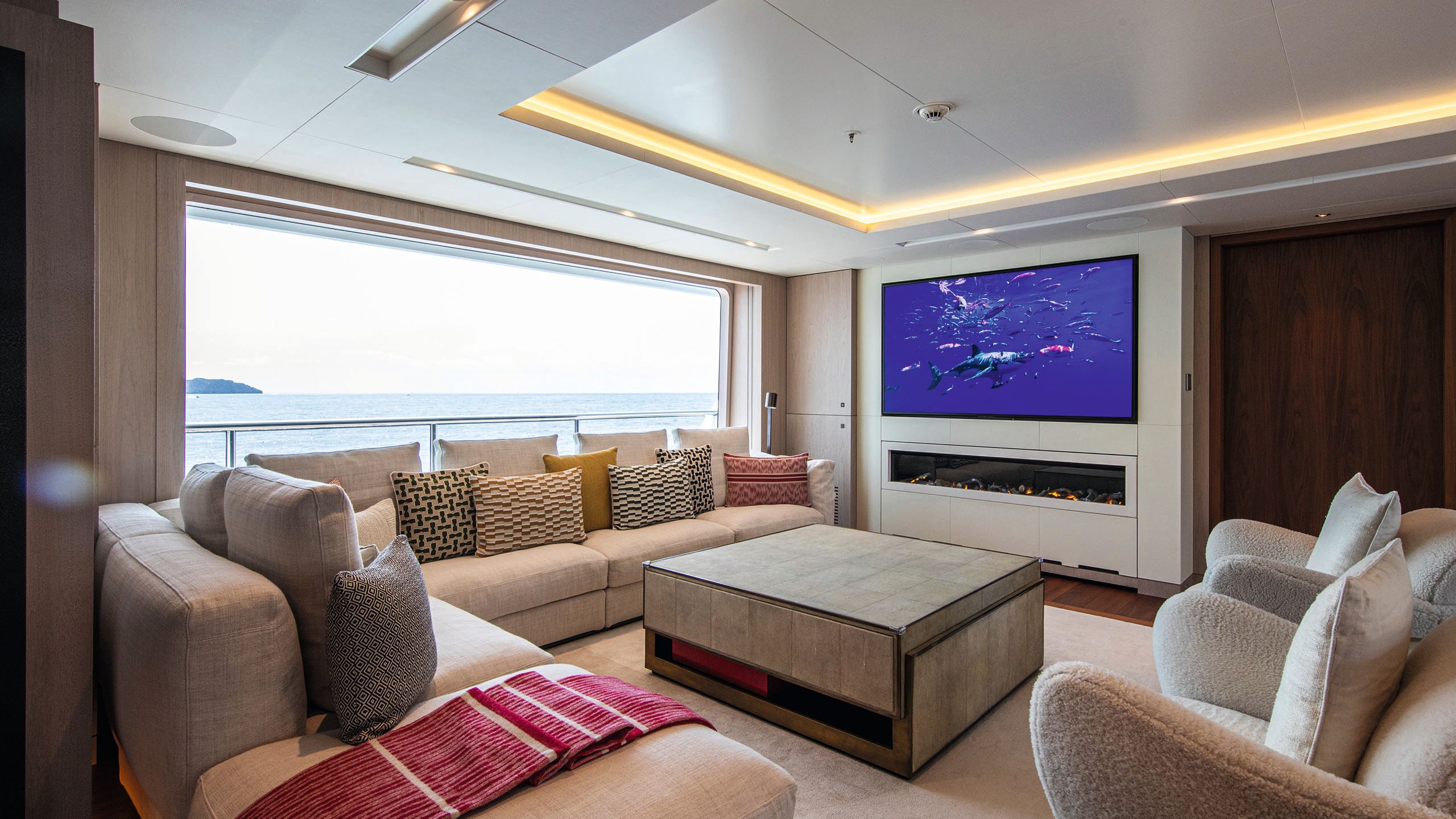 Corner sofa with large centrepiece coffee table and two armchairs. A TV is set in the wall with a horizontal fireplace underneath