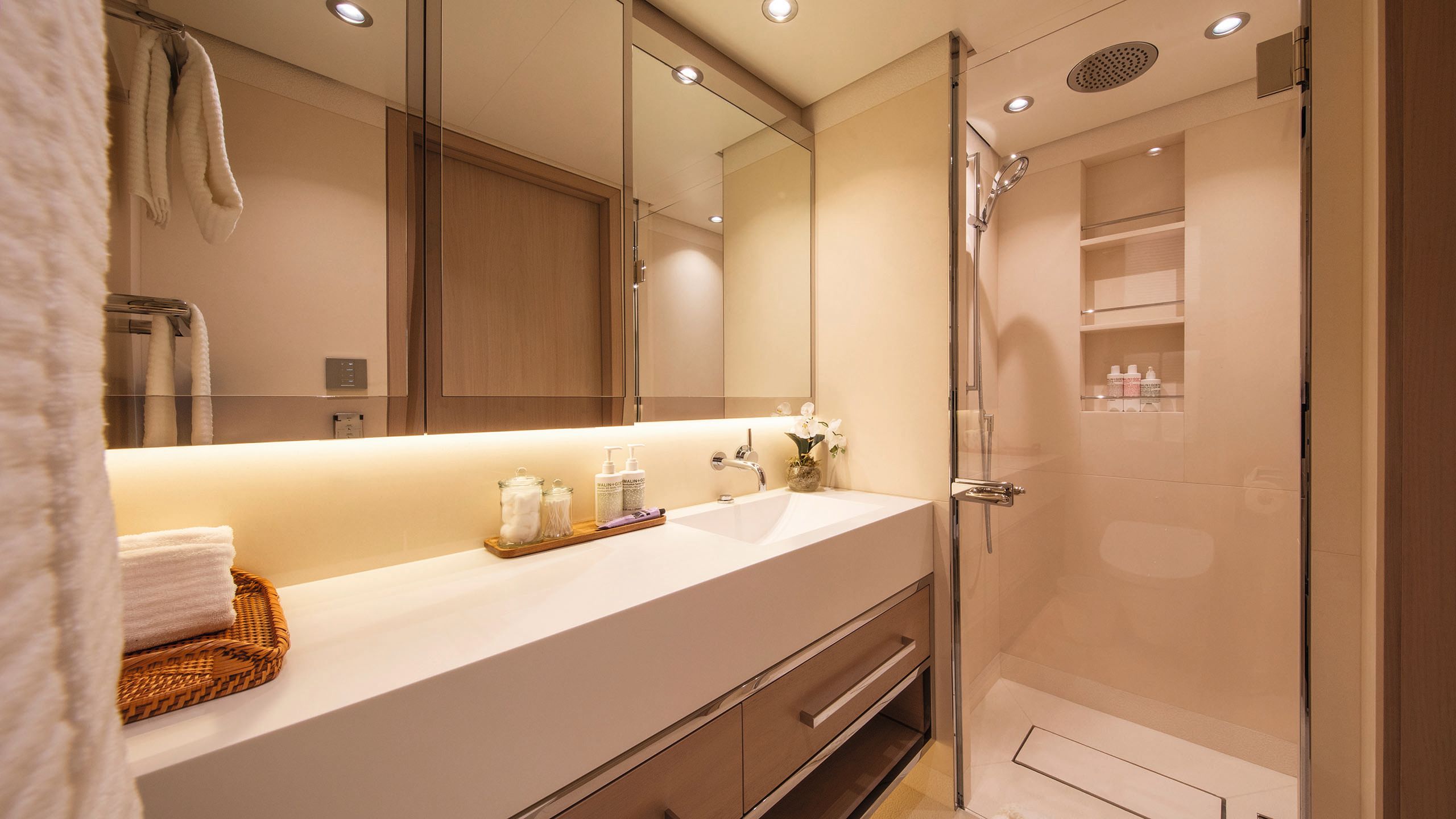 View of a bathroom with glass shower cubicle at one end. It's done in neutral colours and chrome fittings
