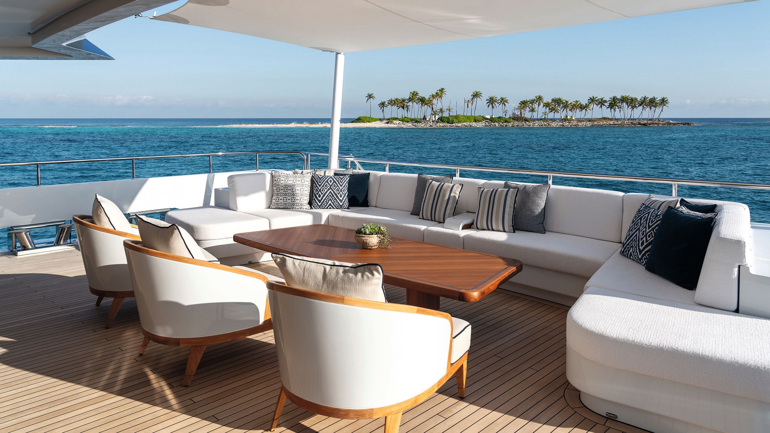 A brown coffee table on a covered area of the deck, surrounded by a white u-shaped sofa and three armchairs
