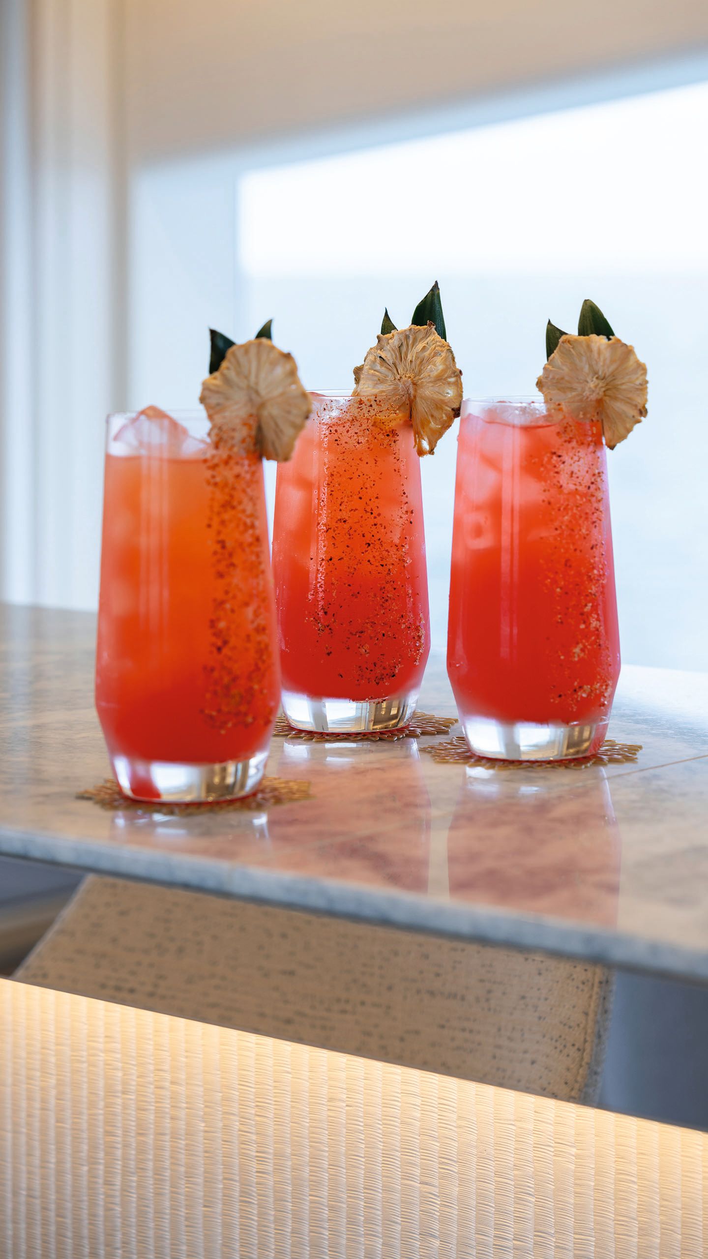 Three tall tumblers on a ledge. They're filled with ice and a bright red drink with dried fruit balanced on the rim