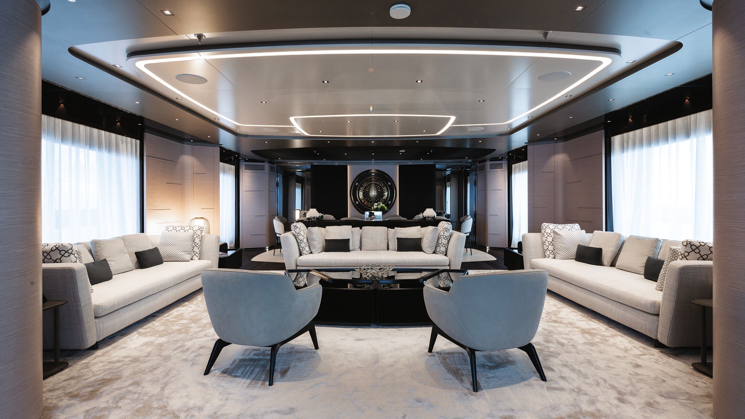 Salon with three white sofas arranged in a U around a large black table and two grey armchairs