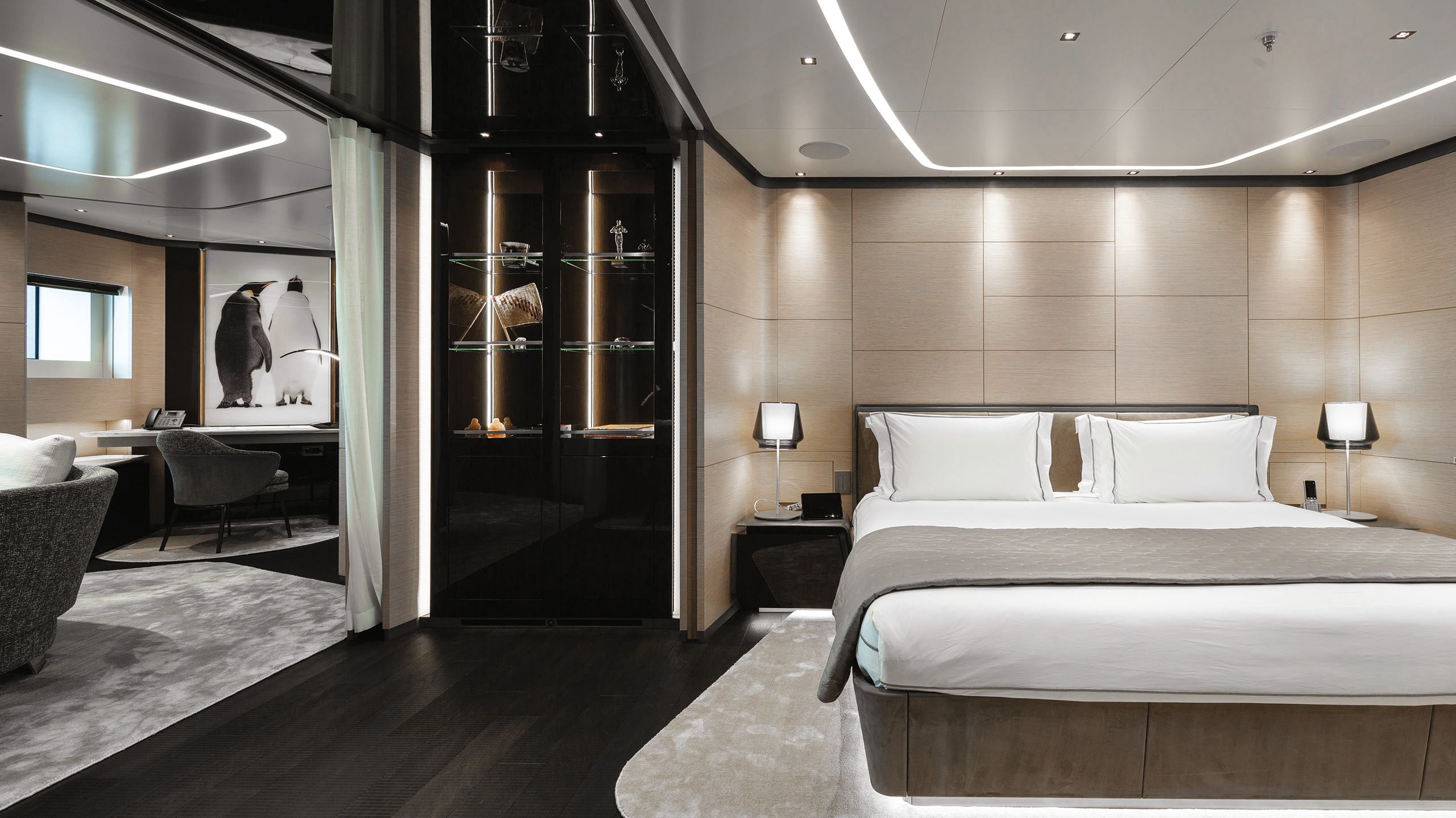 Owner's cabin with large bed made up with neutral linens. To the side is an office and lounge area with a large photo on the wall of two penguins