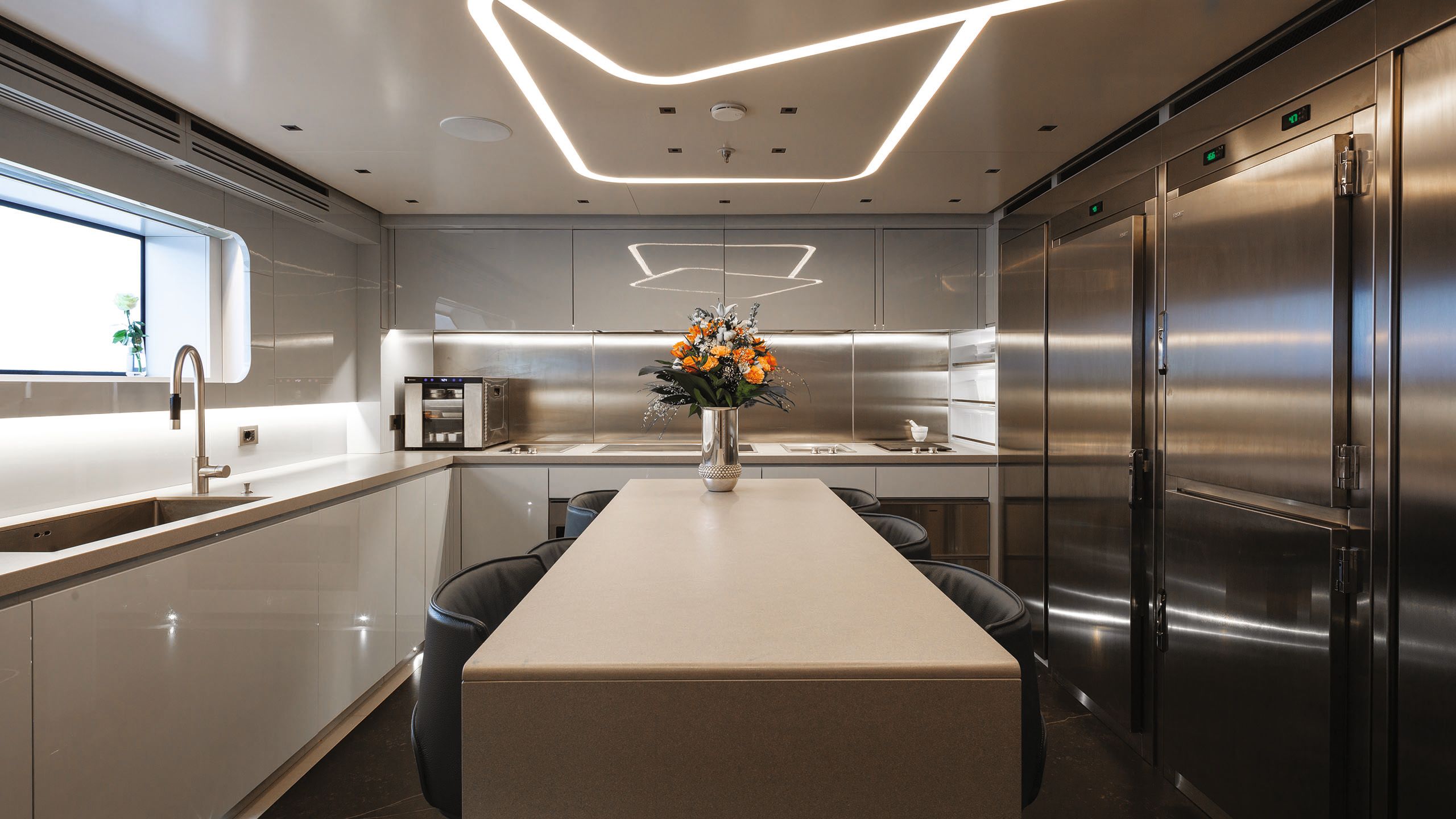 View of the kitchen looking down a central counter in neutral colour-scheme with brushed metalwork