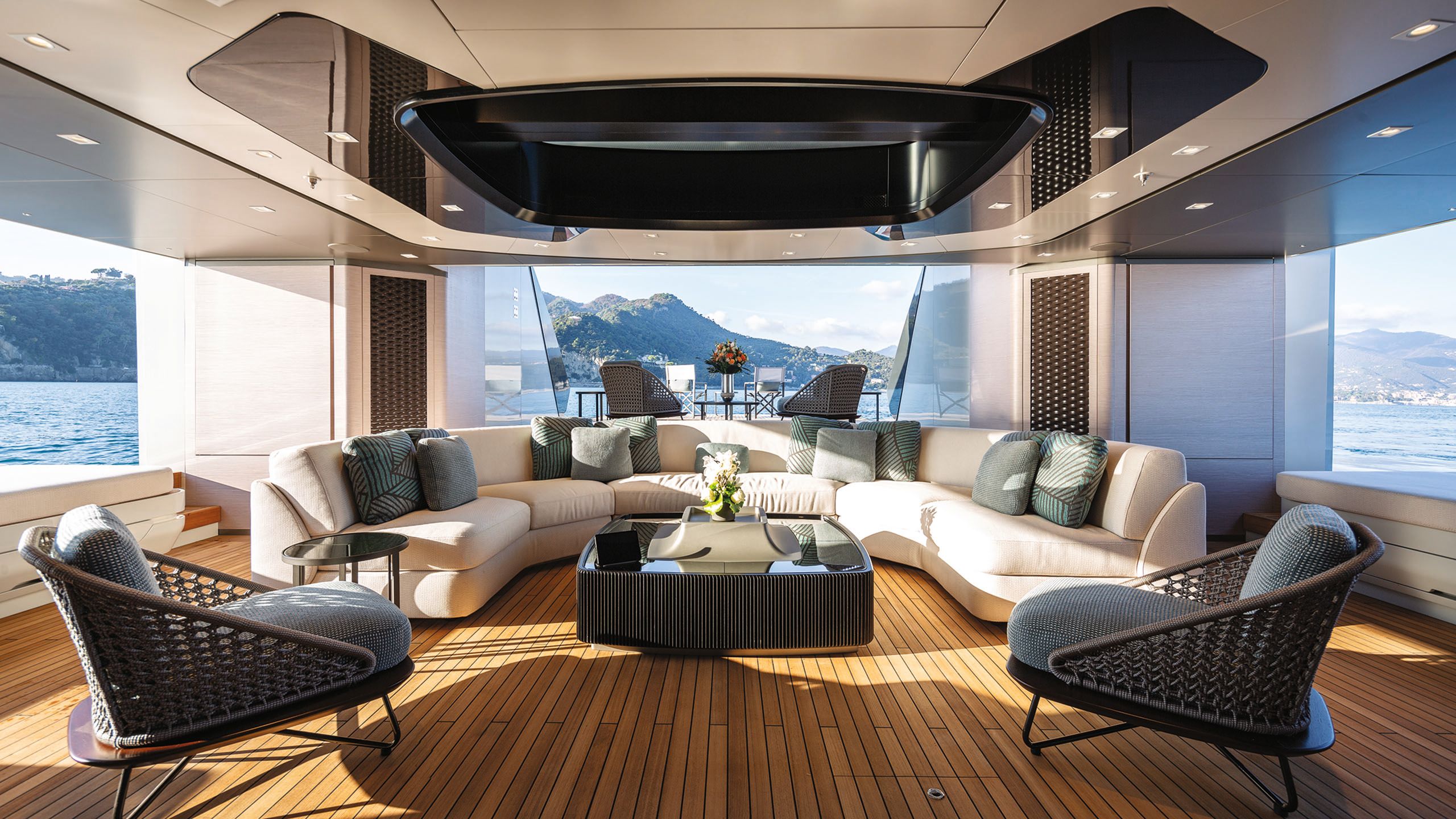 Large curved cream sofa and rattan chairs with grey cushion pads inside a room with windows on three sides
