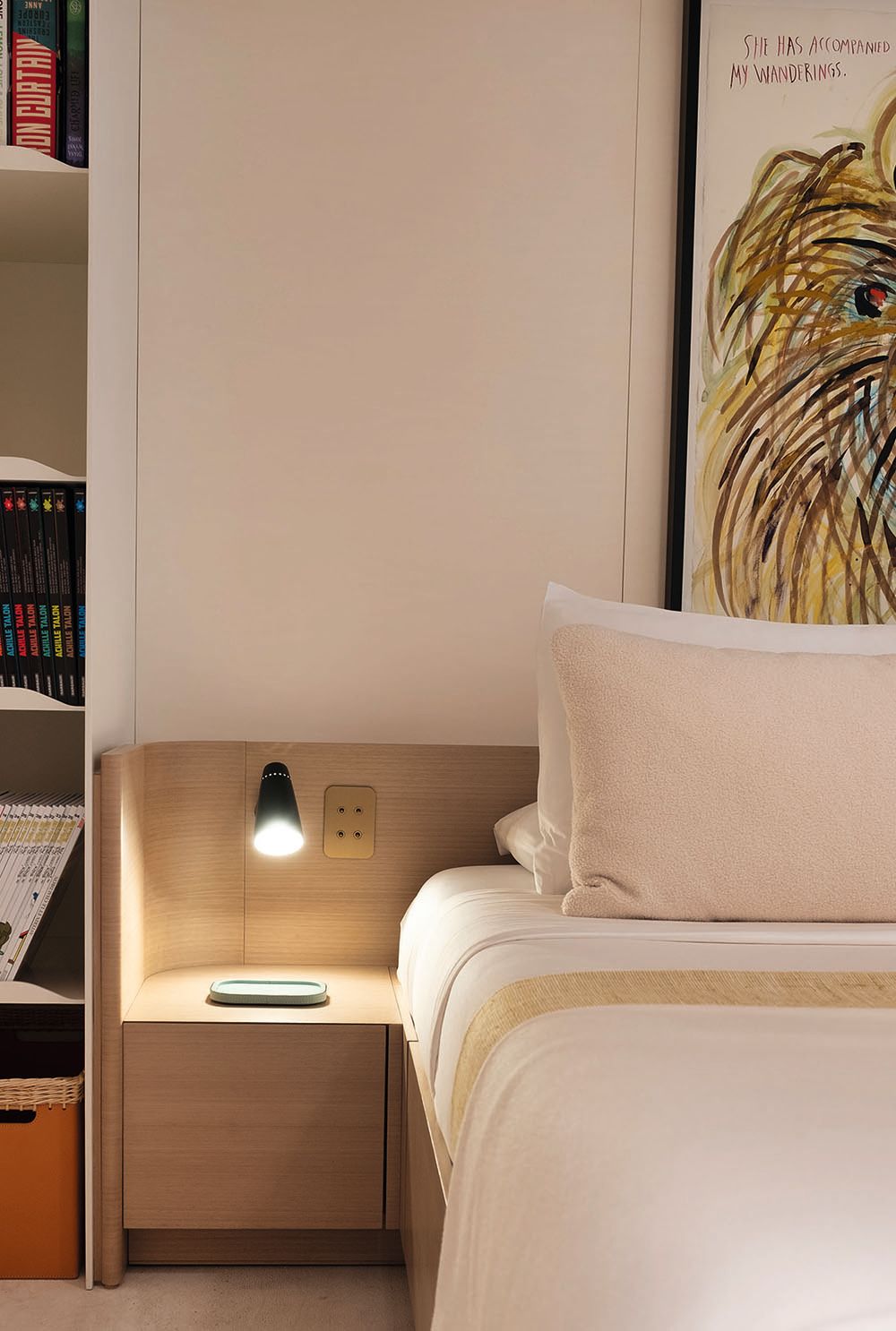 Partial side view of a bed with bedside lamp. A picture of a lion hangs over the headboard