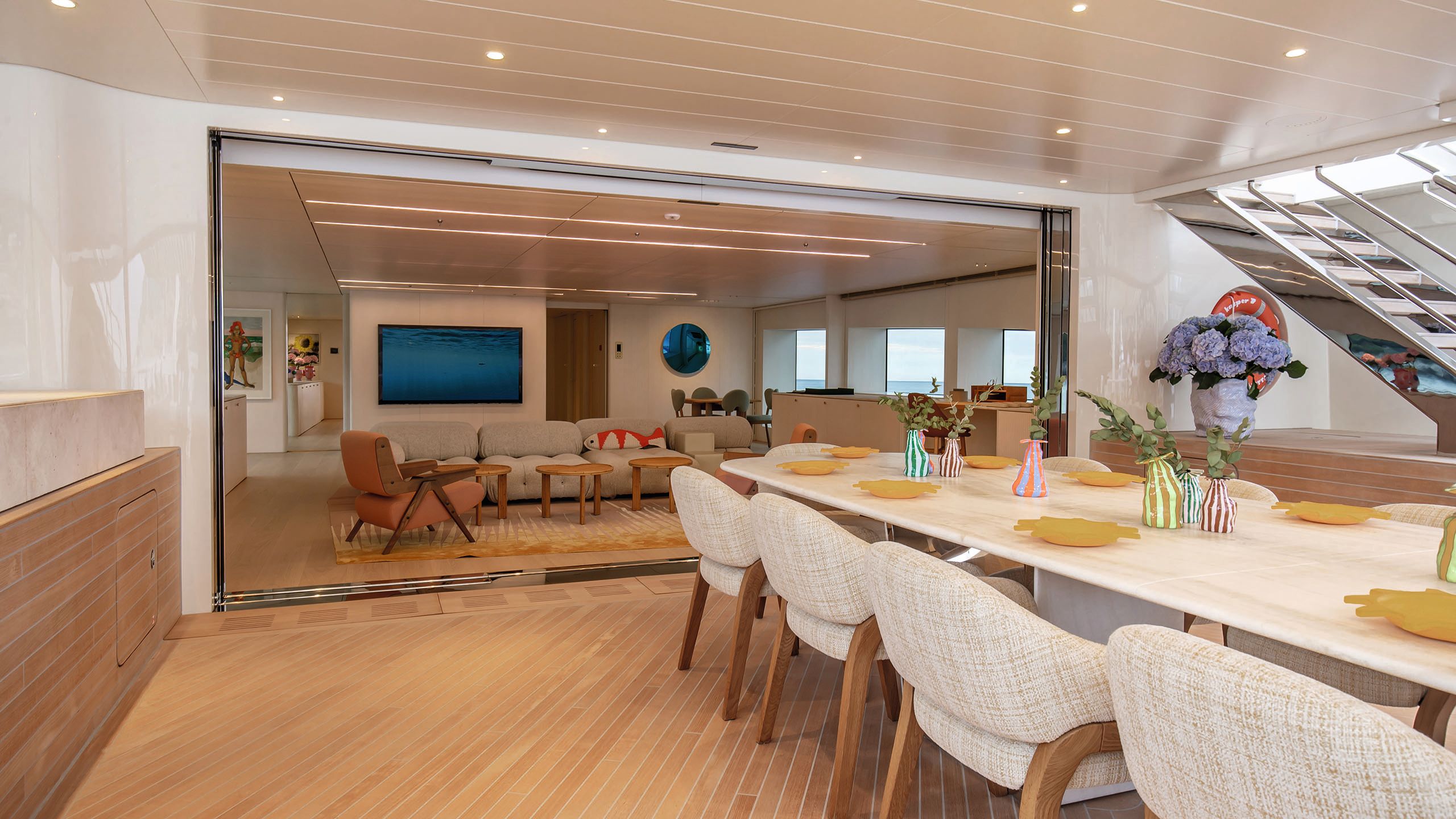 A view of the upper deck lounge taken from the deck, which has a long white dining table and chairs upholstered in cream melange fabric