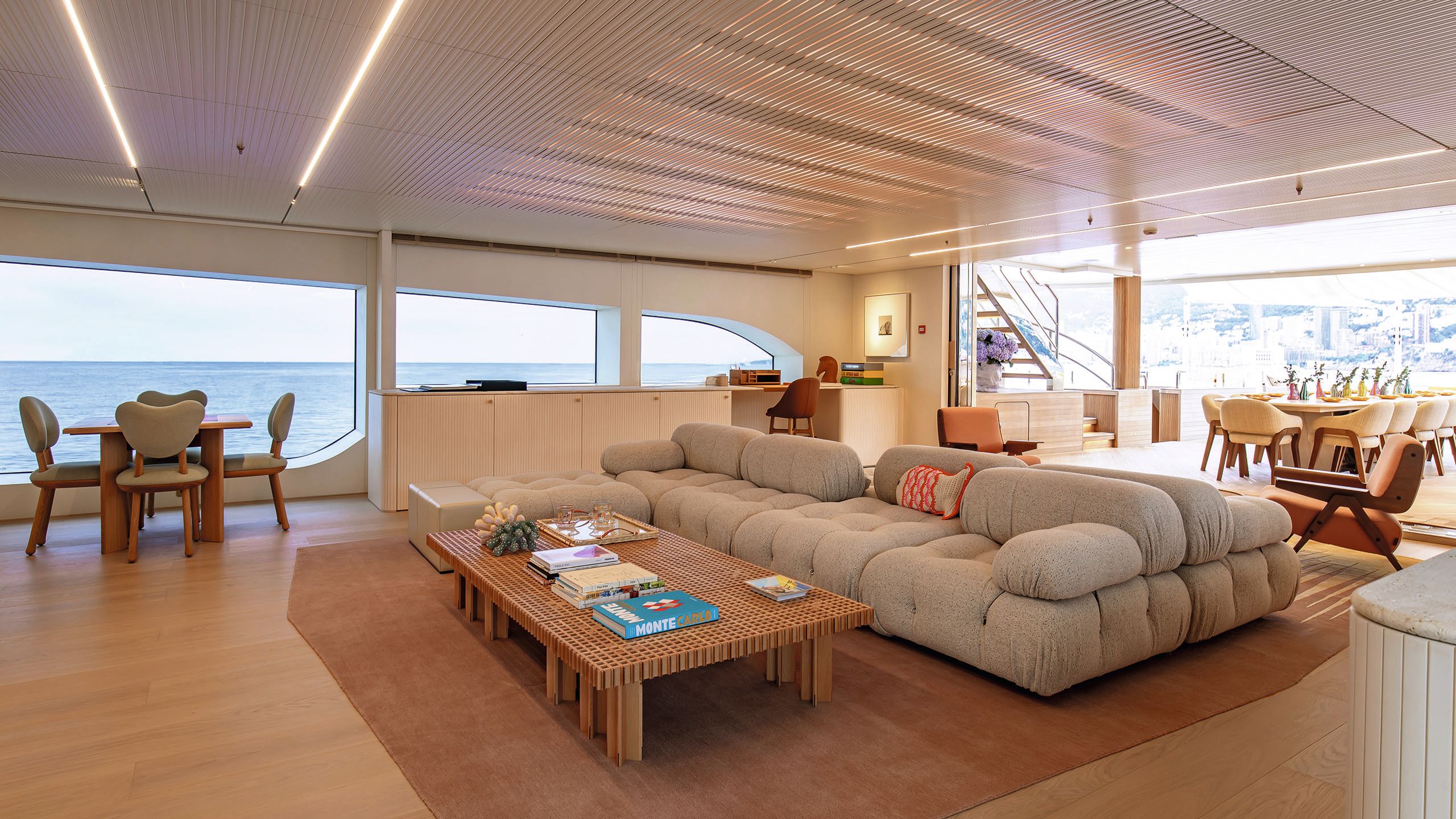 The upper deck lounge has a large "bubble-like" corner sofa in the centre on a rug with large wooden coffee table in front. To the side is a table with chairs that have heart-shaped backs